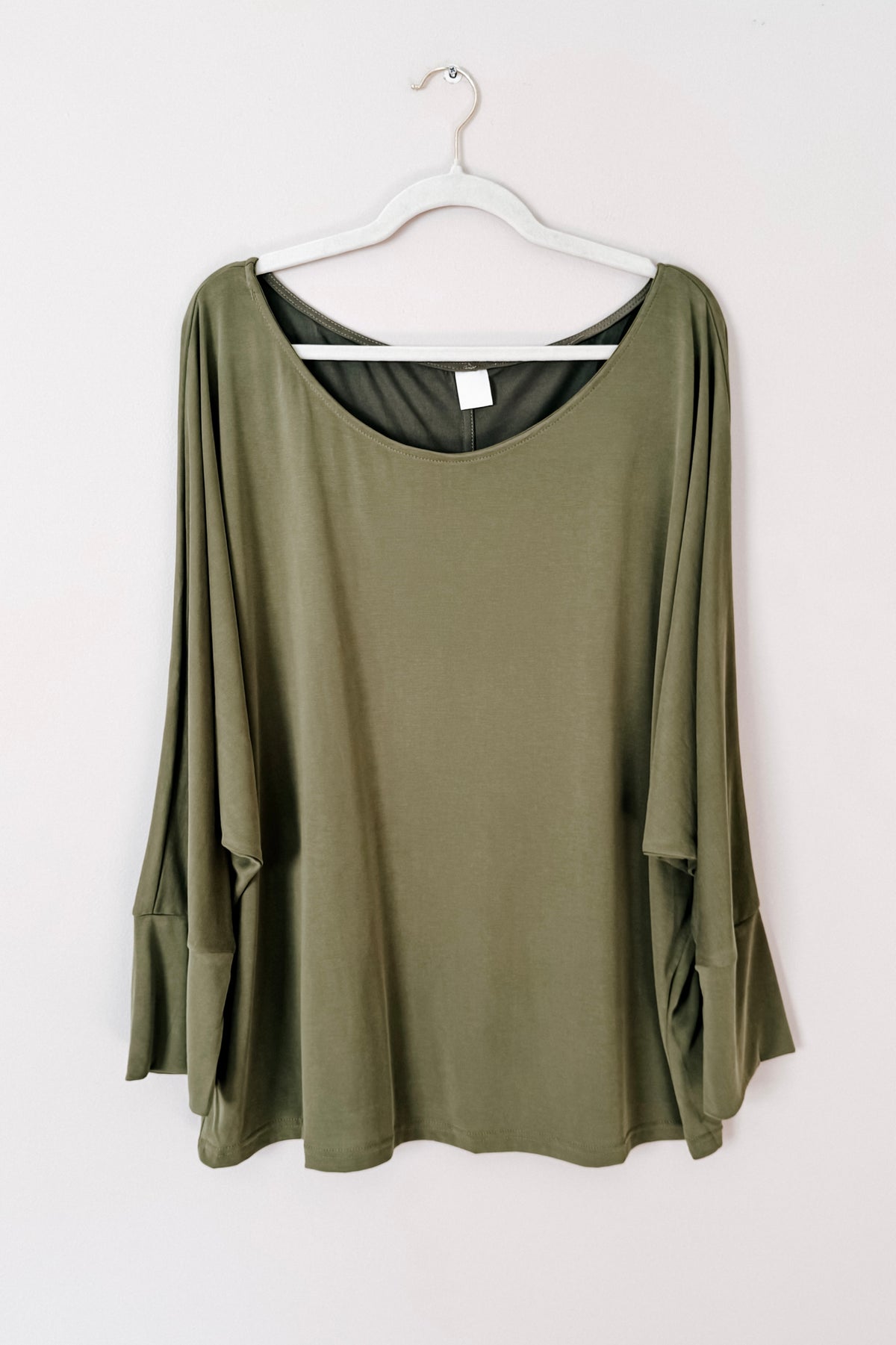 Green brushed microfiber top with a boat neckline dolman sleeves and exaggerated cuffs displayed on a white hanger