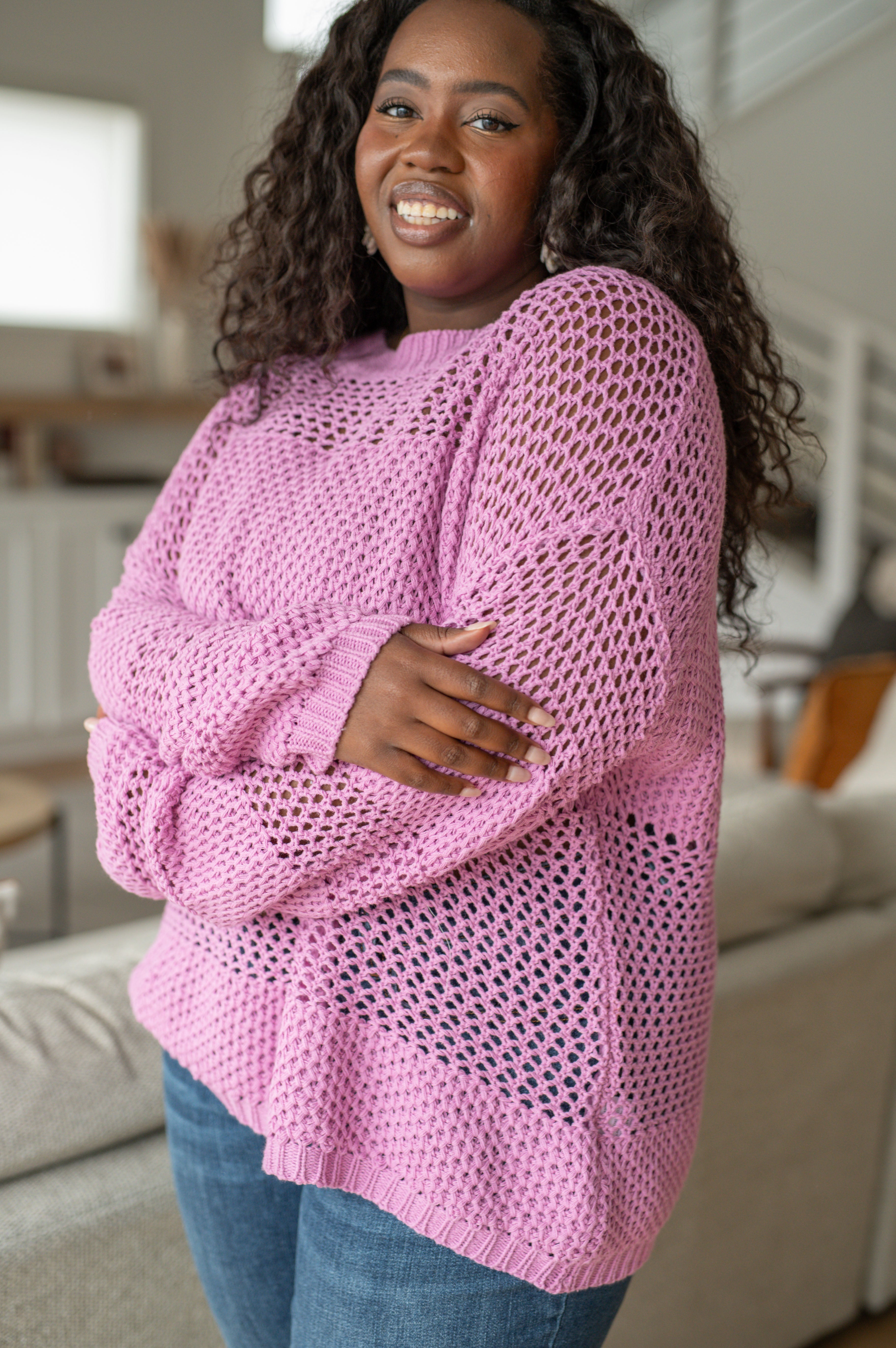 Smiling plus-size woman wearing a loose lavender open knit sweater with blue jeans standing indoors