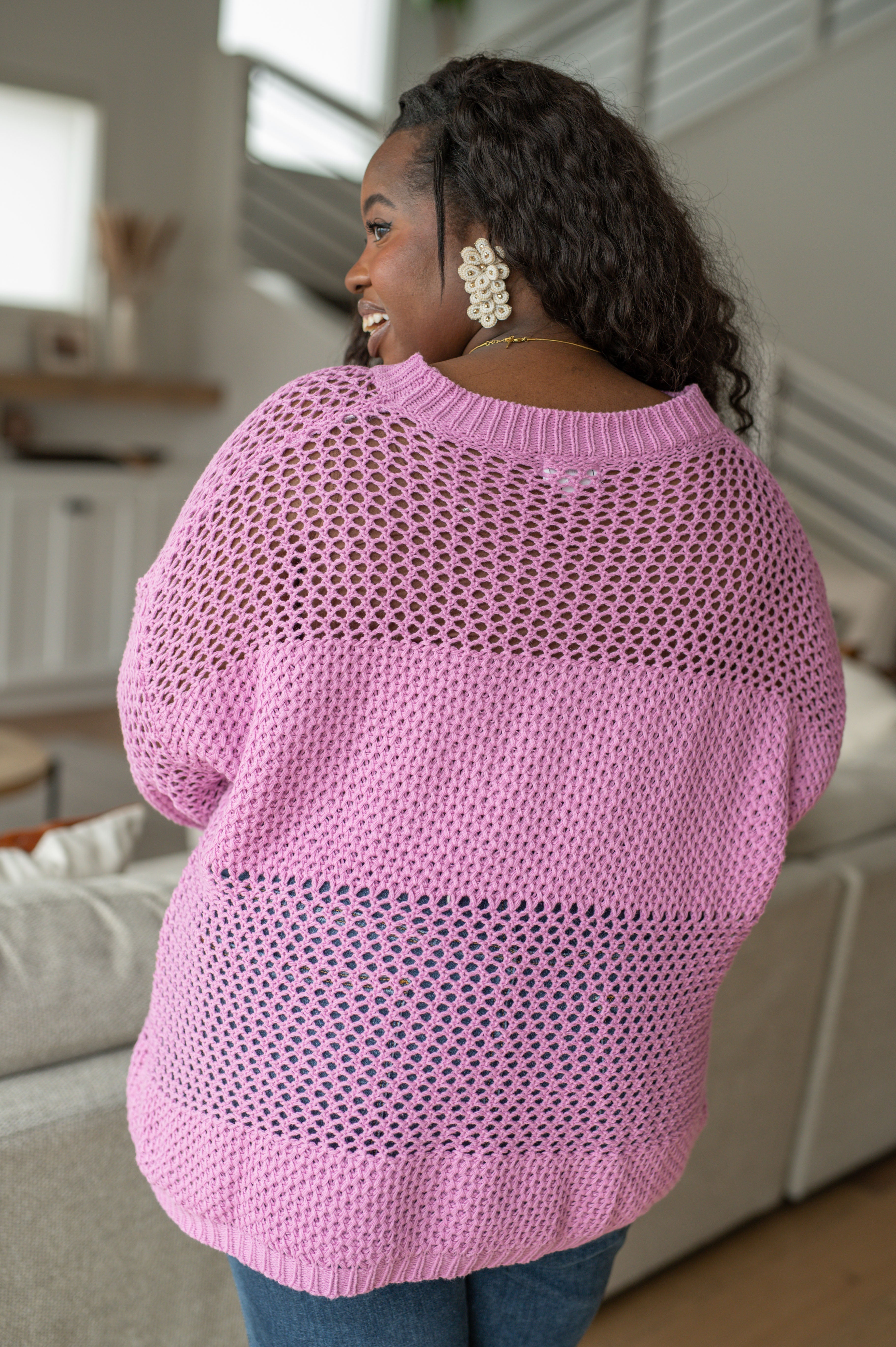 Black woman with curly hair wearing a loose pink knit sweater with open weave detail indoors