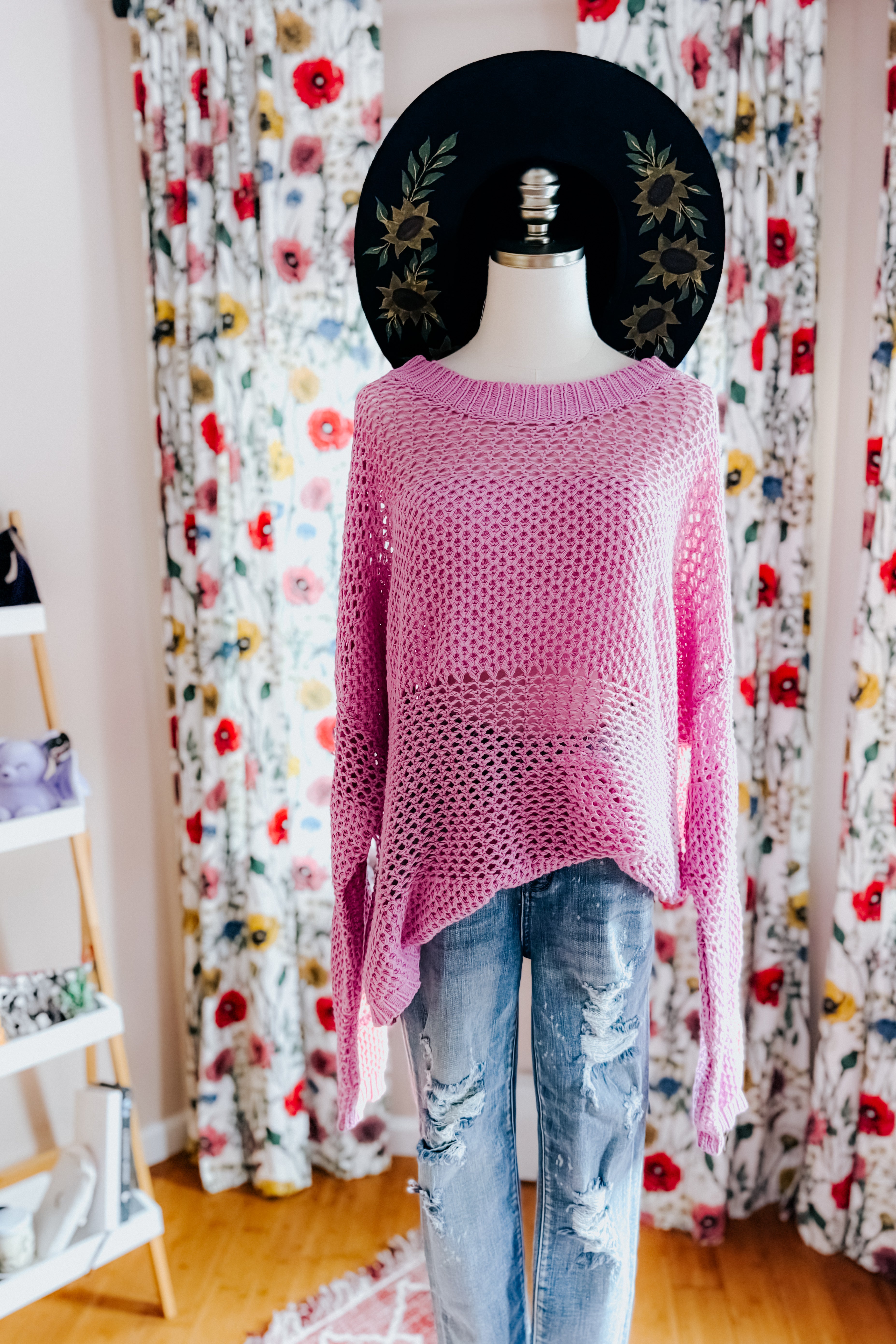 Loose pink knit sweater with open weave detail displayed on mannequin wearing distressed jeans indoors