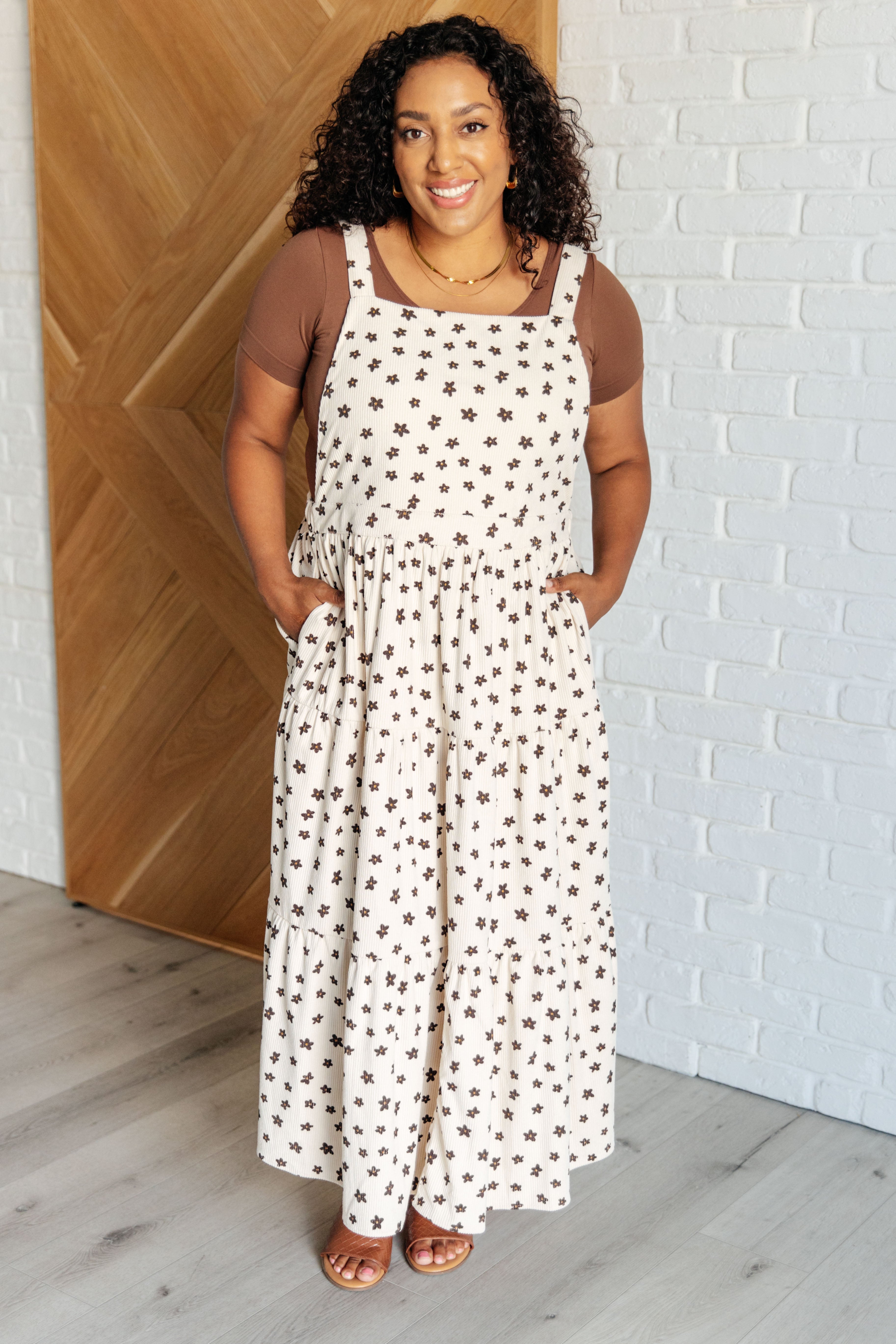 Smiling woman wearing a cream sleeveless dress with small dark floral print over a brown short-sleeve top indoors