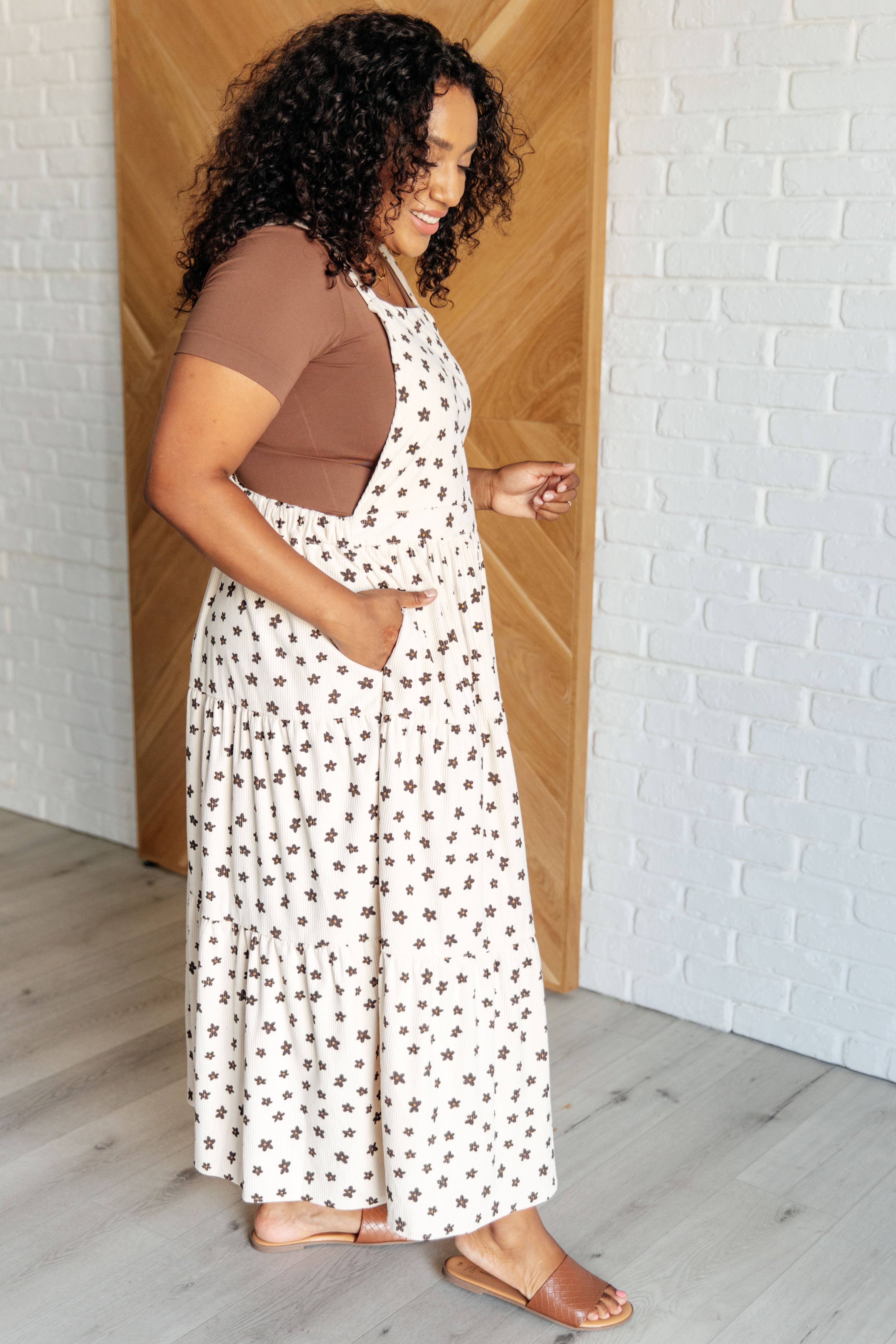 Woman with curly hair wearing a cream long dress with dark star print and a brown short-sleeve top indoors