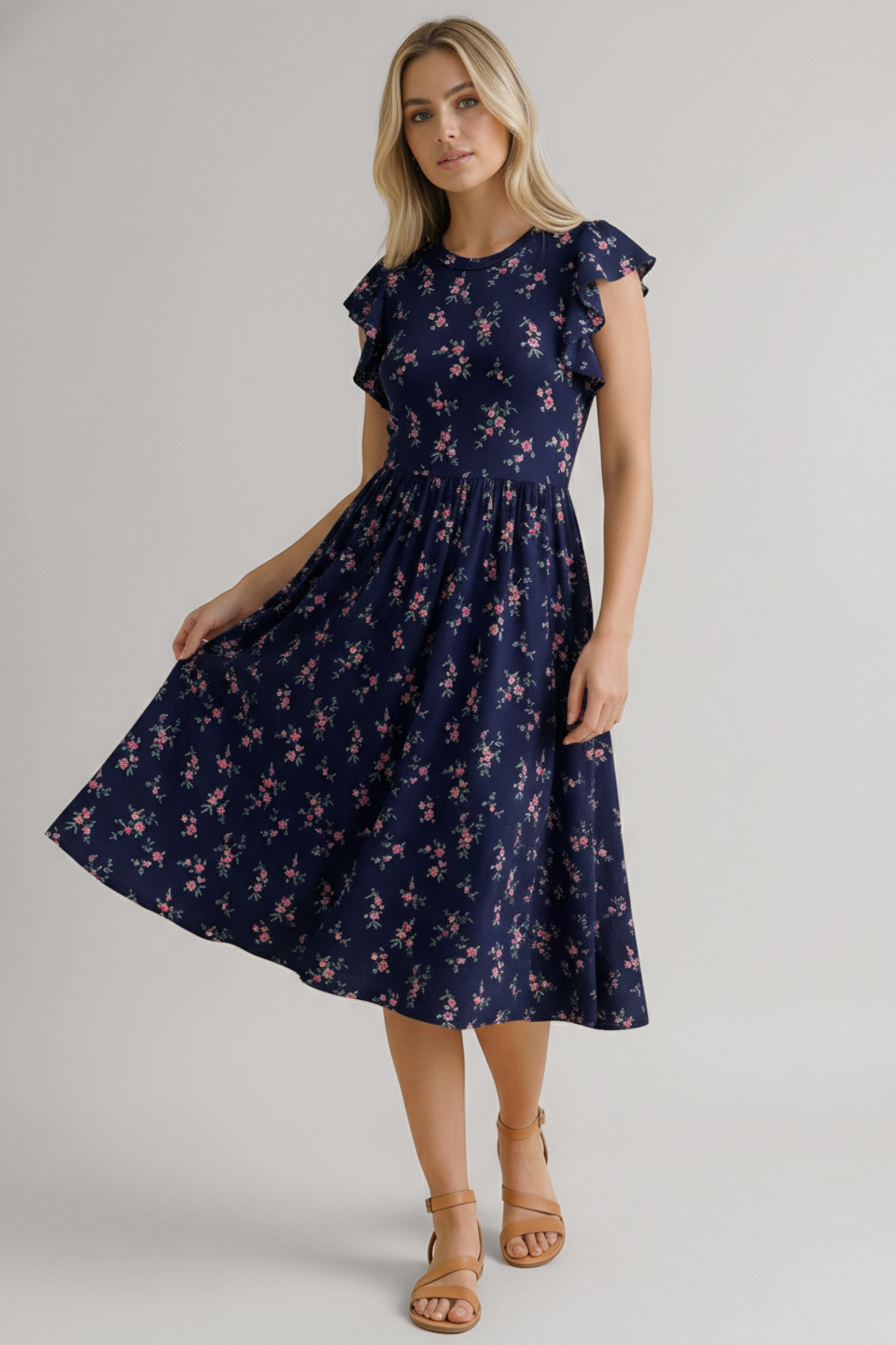 Woman wearing a navy dress with pink floral details, ruffled cap sleeves, and a flowing midi skirt paired with tan sandals
