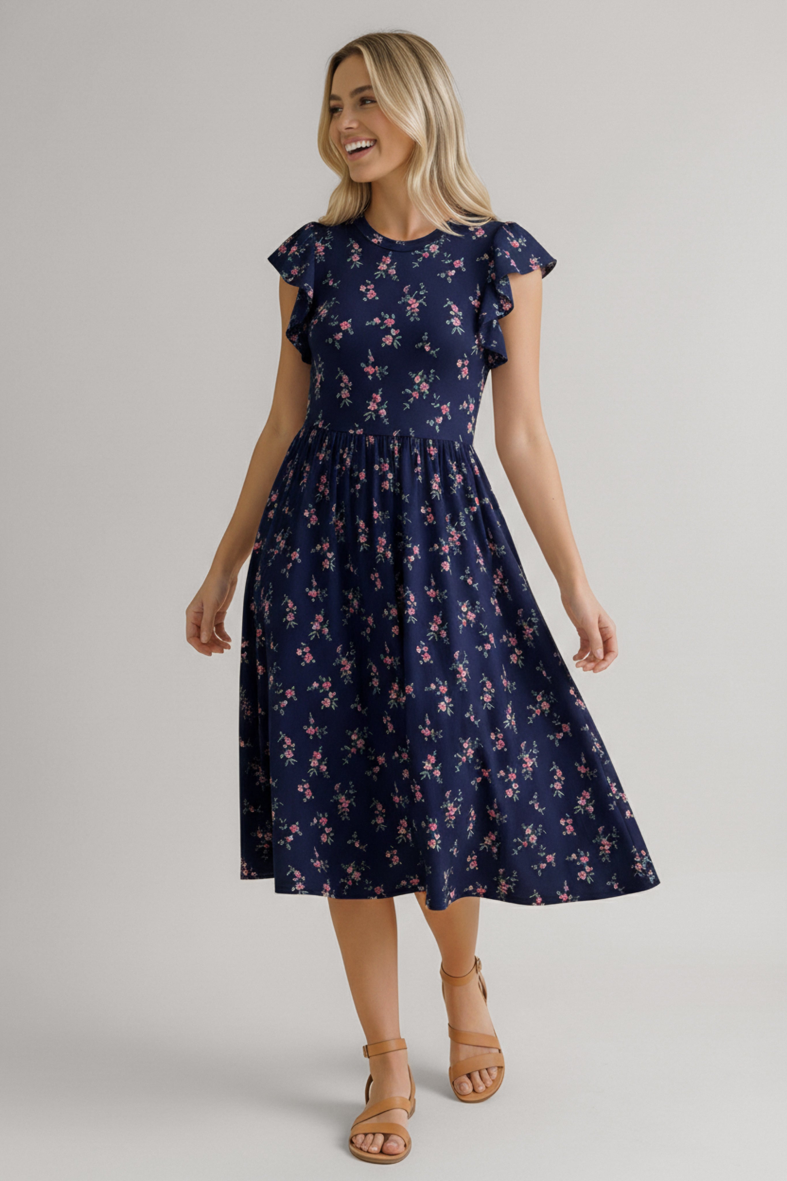 Woman wearing a navy dress with pink floral pattern, ruffled short sleeves, and a flowing midi skirt paired with tan sandals