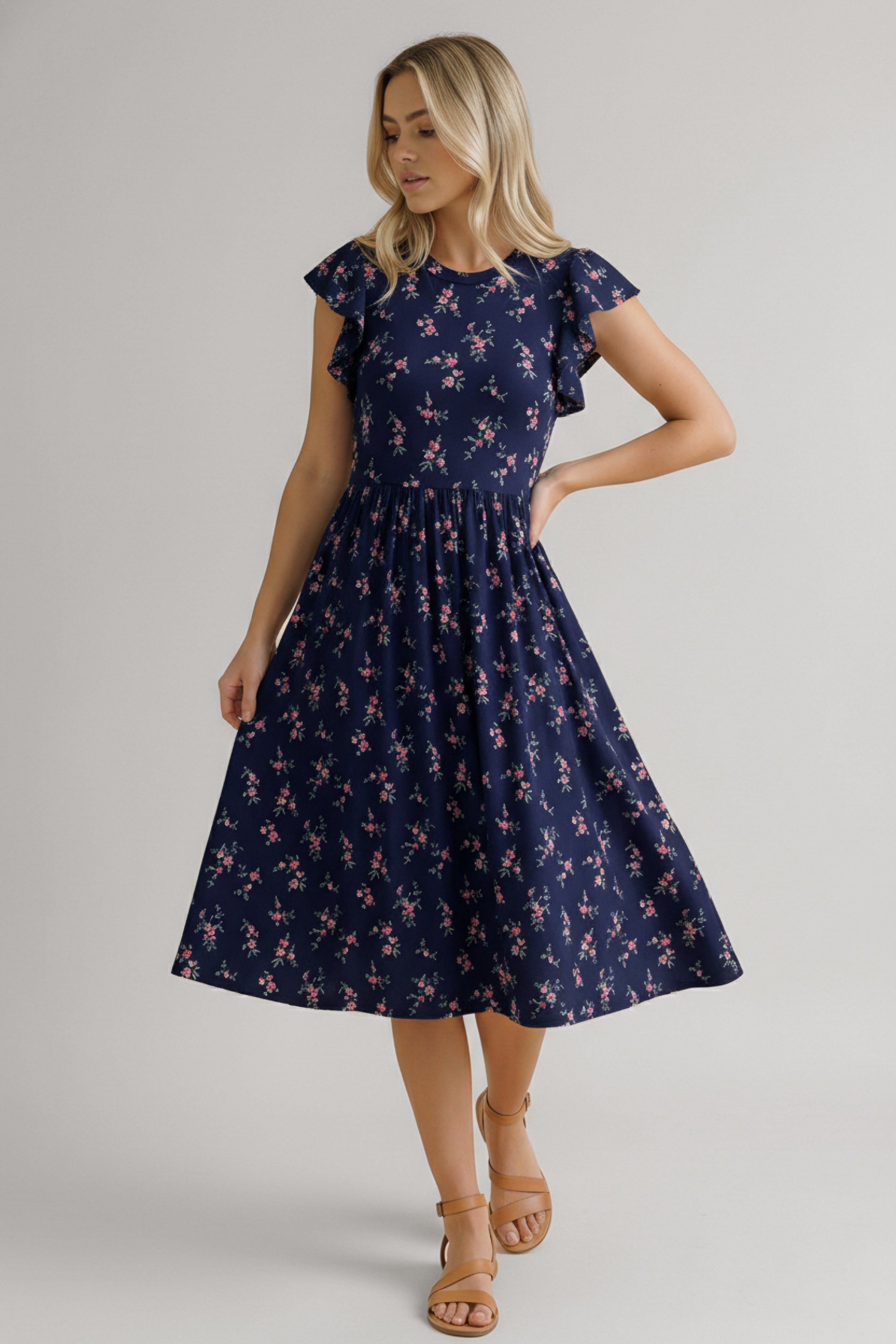 Woman wearing a navy dress with small pink floral print, flutter sleeves, and a midi gathered skirt paired with tan sandals