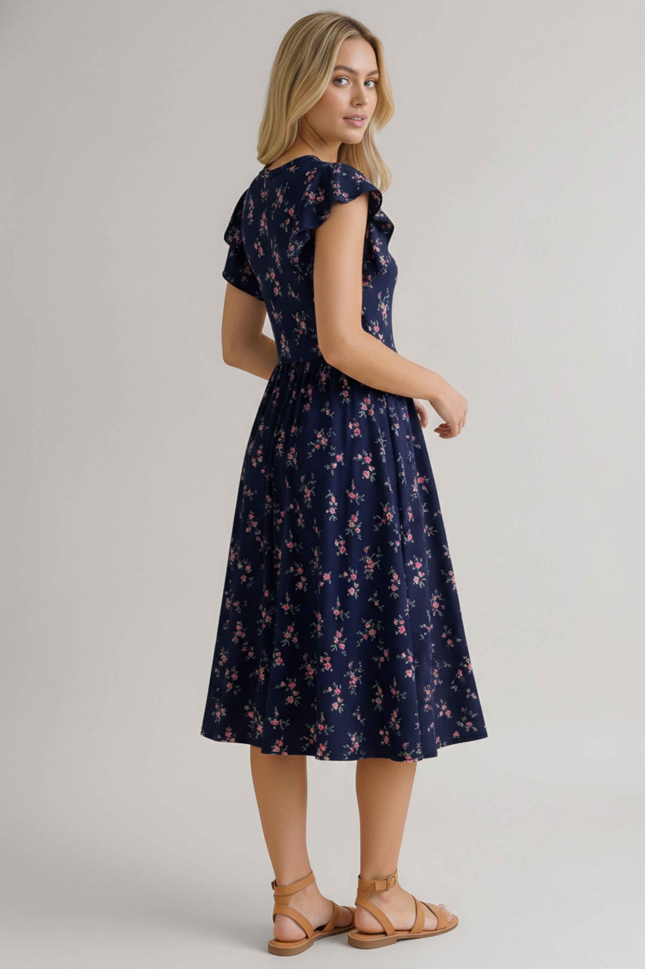 Woman wearing a navy dress with a small floral pattern, flutter sleeves, and a gathered skirt shown from the back