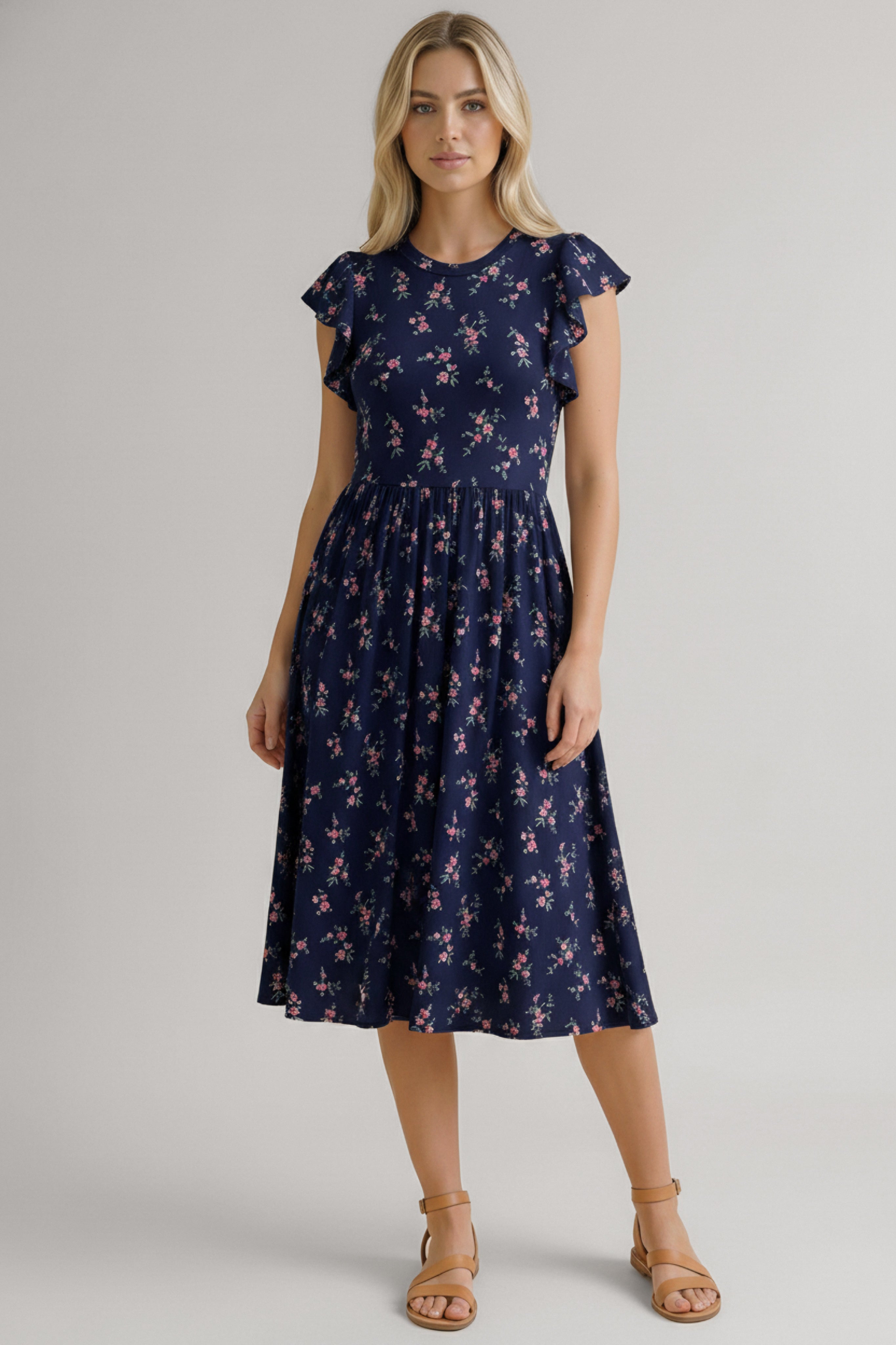 Woman wearing a navy dress with small pink floral print, flutter sleeves, and a gathered midi skirt paired with tan sandals