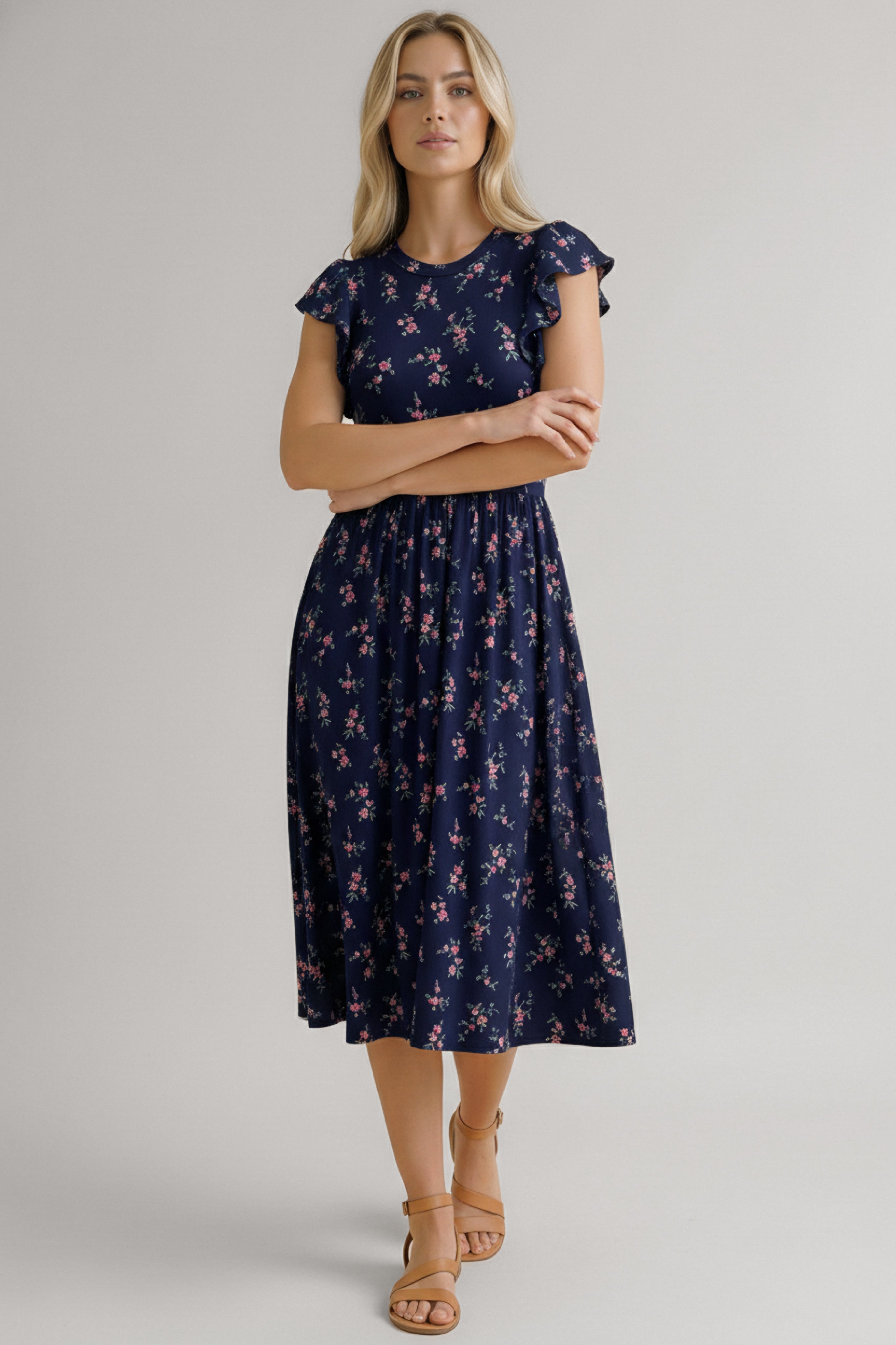 Woman wearing a navy dress with small pink floral print, flutter sleeves, and a gathered waist paired with tan sandals