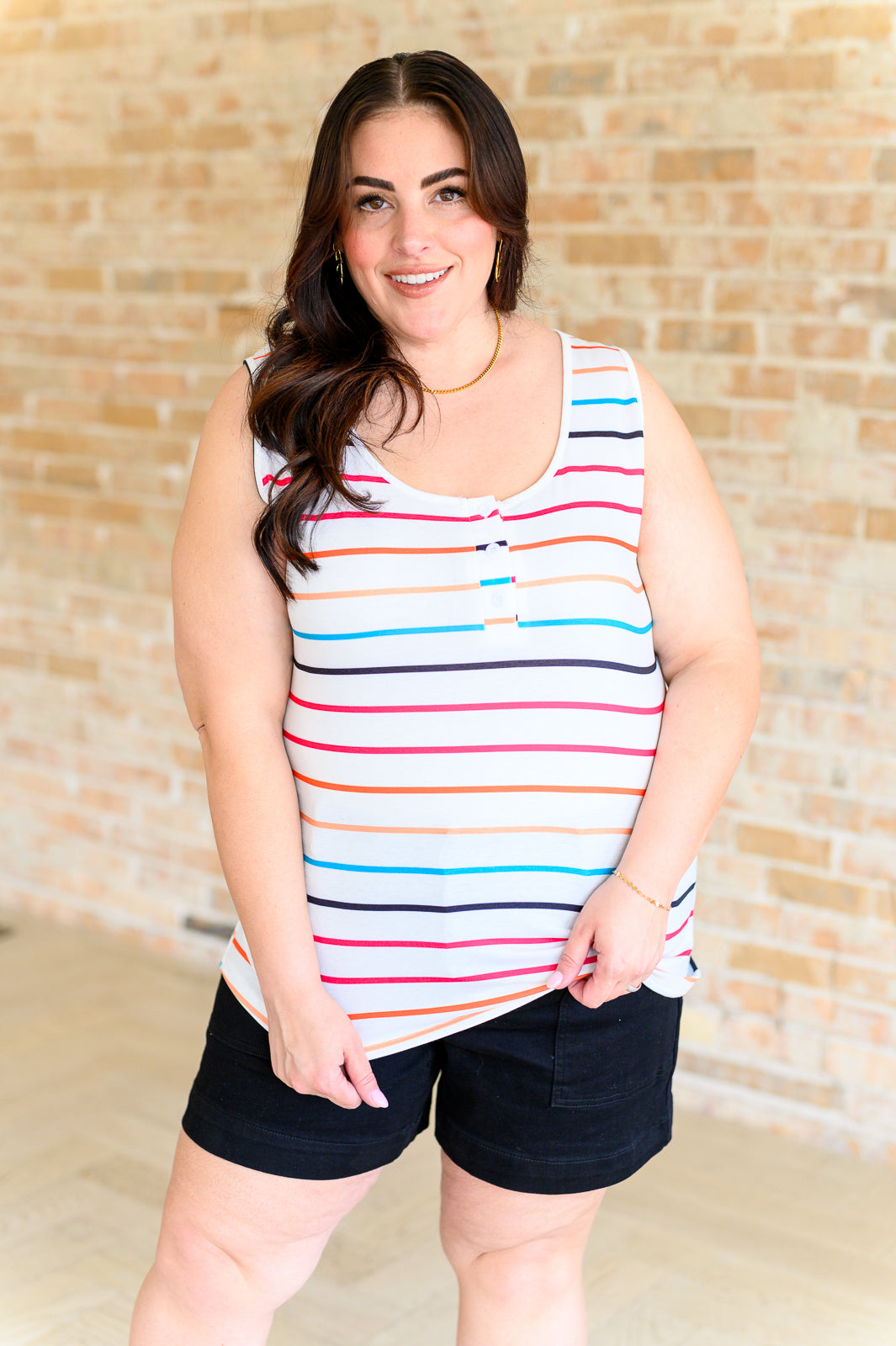 Plus size woman wearing ivory sleeveless henley tank with colorful stripes and black shorts, smiling indoors