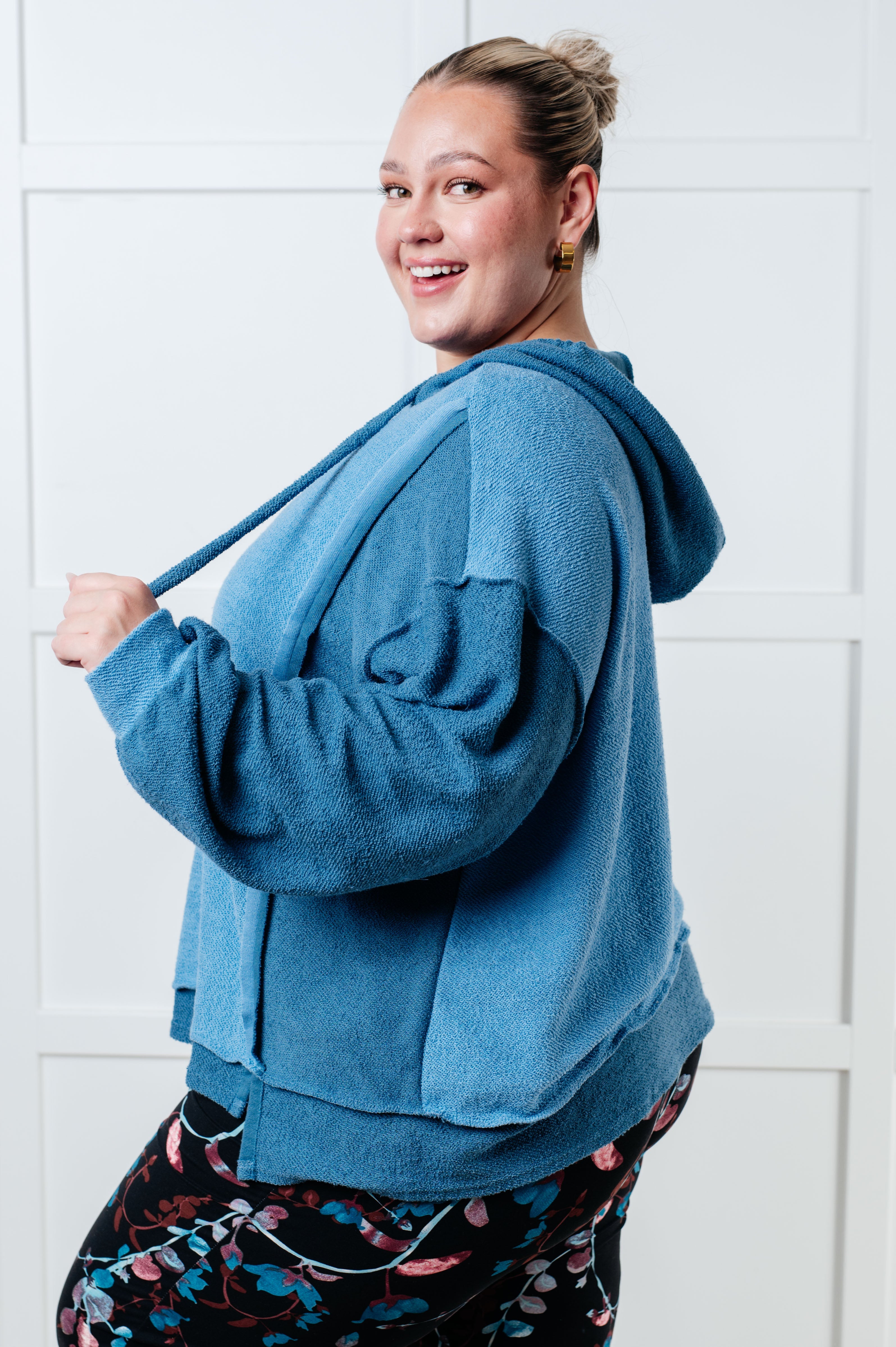 Smiling woman wearing a relaxed fit blue color block hoodie with textured fabric and a hood, paired with floral print leggings indoors.