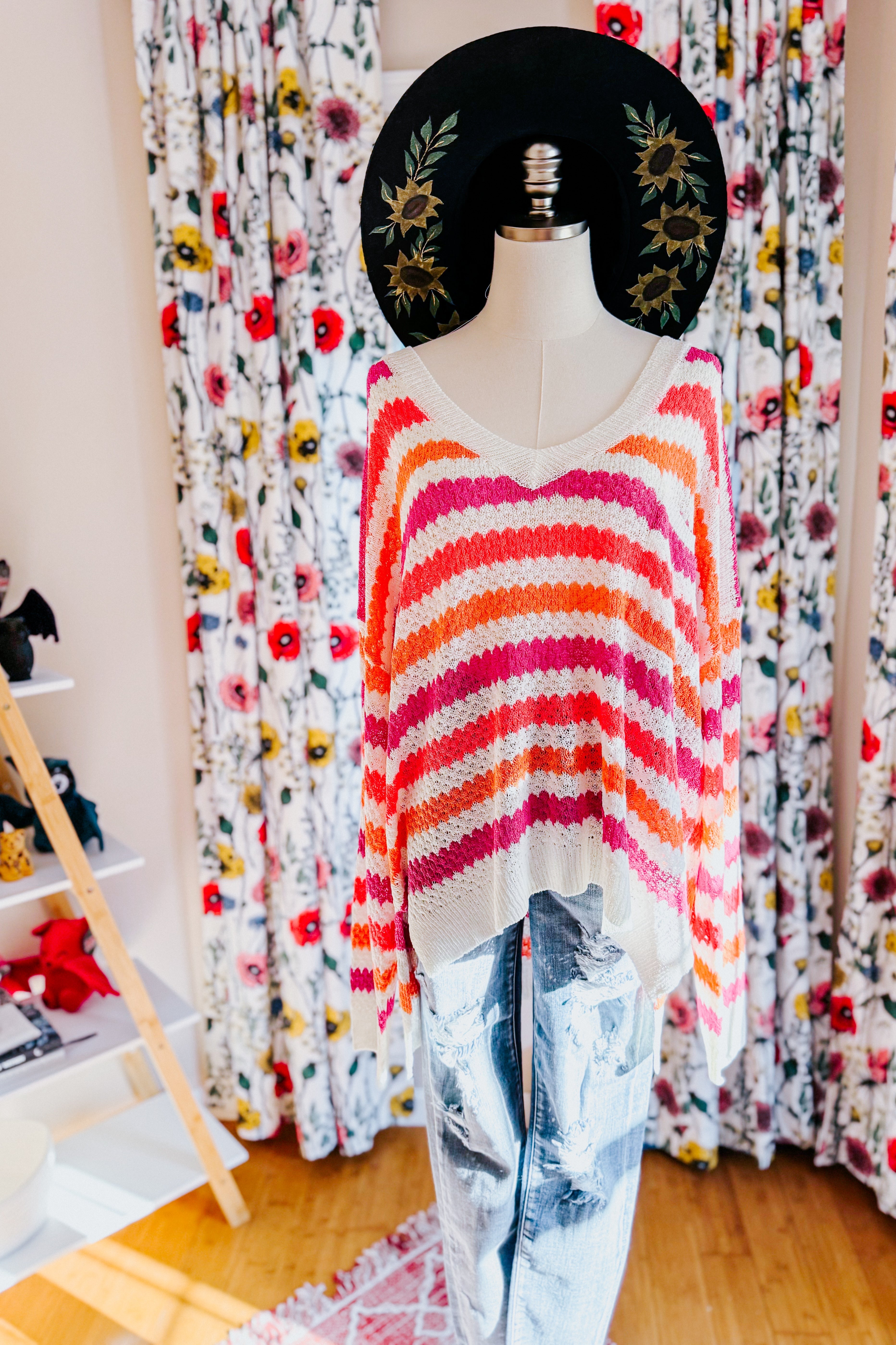 Mannequin dressed in a striped drop shoulder sweater in pink and orange tones paired with light blue distressed jeans, standing indoors.