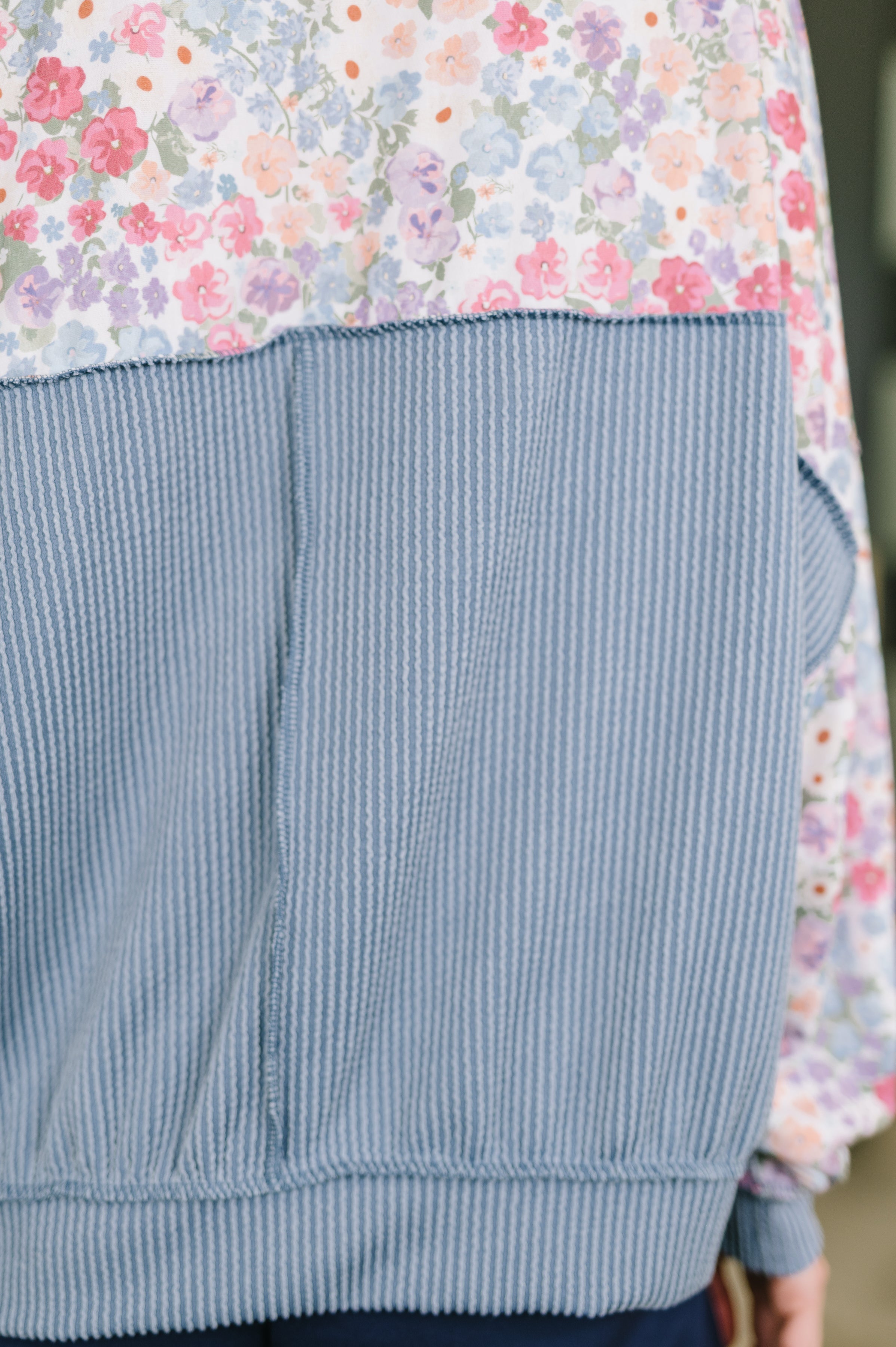 Close-up of blue ribbed fabric on lower back of floral patterned pullover with soft pastel flowers