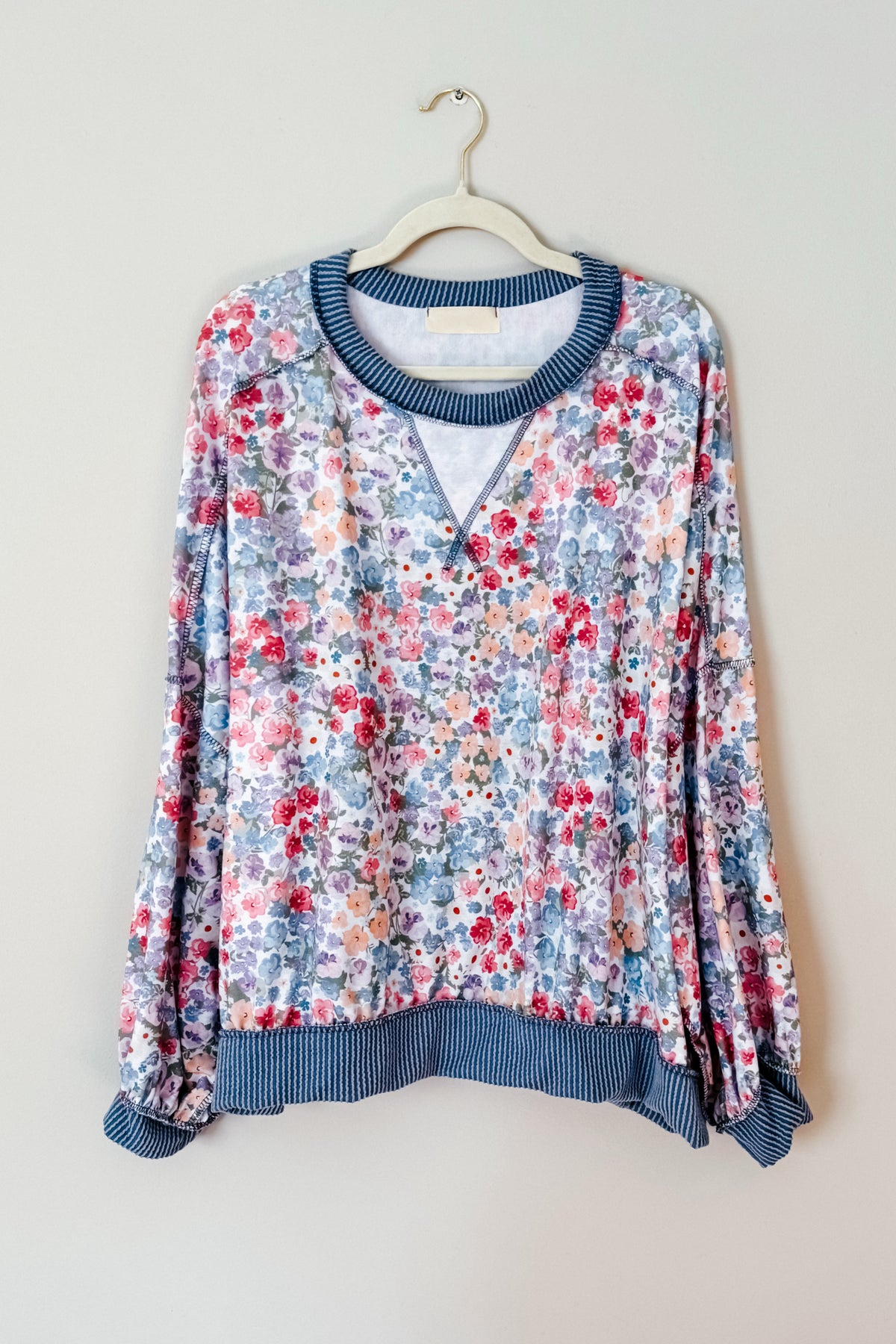 Blue floral drop shoulder pullover with a round cable ribbed neckline and ribbed cuffs and hem hanging on a hanger