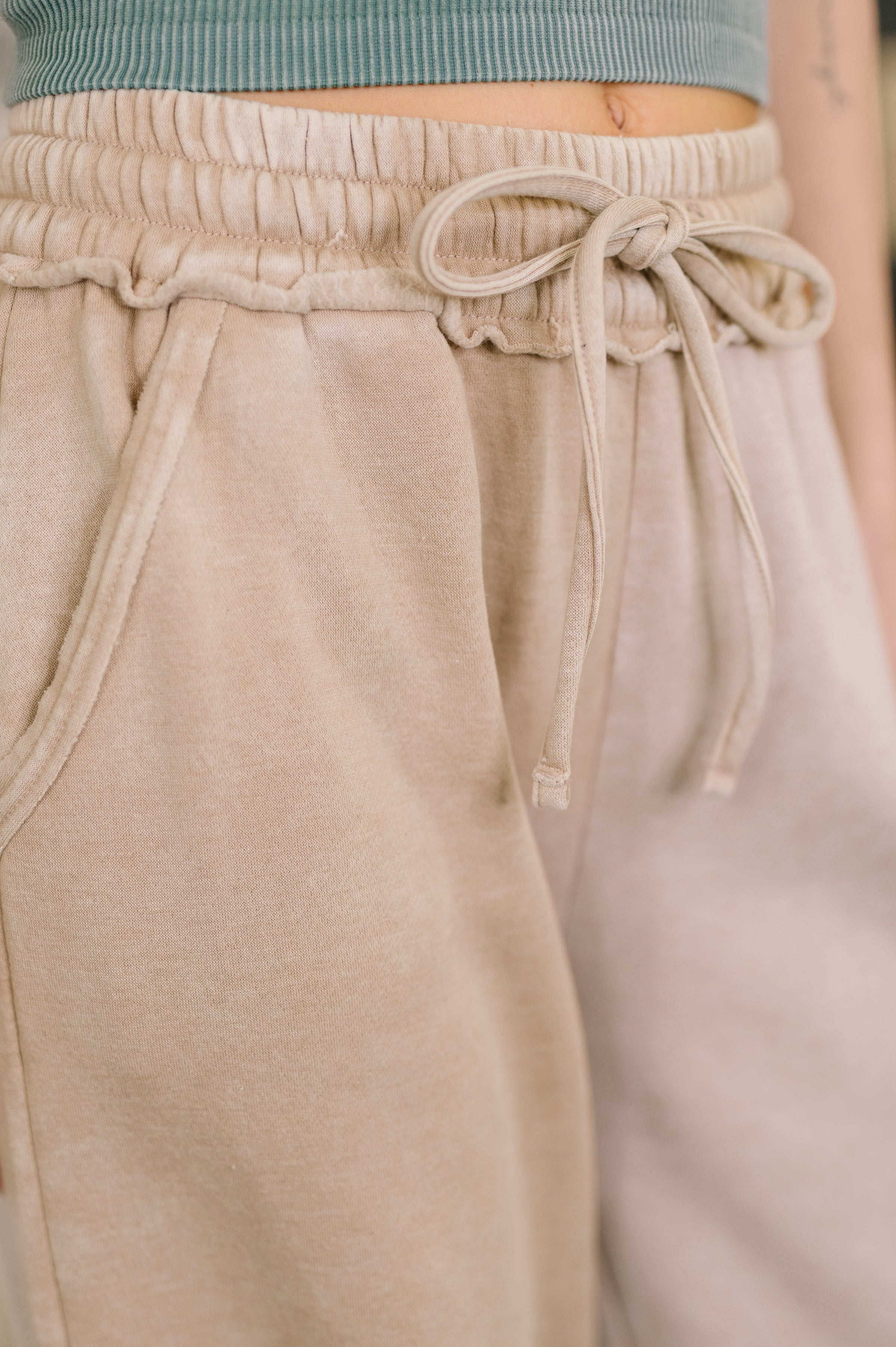 Close-up of ash mocha high waist palazzo sweatpants with drawstring and side pocket detail worn indoors