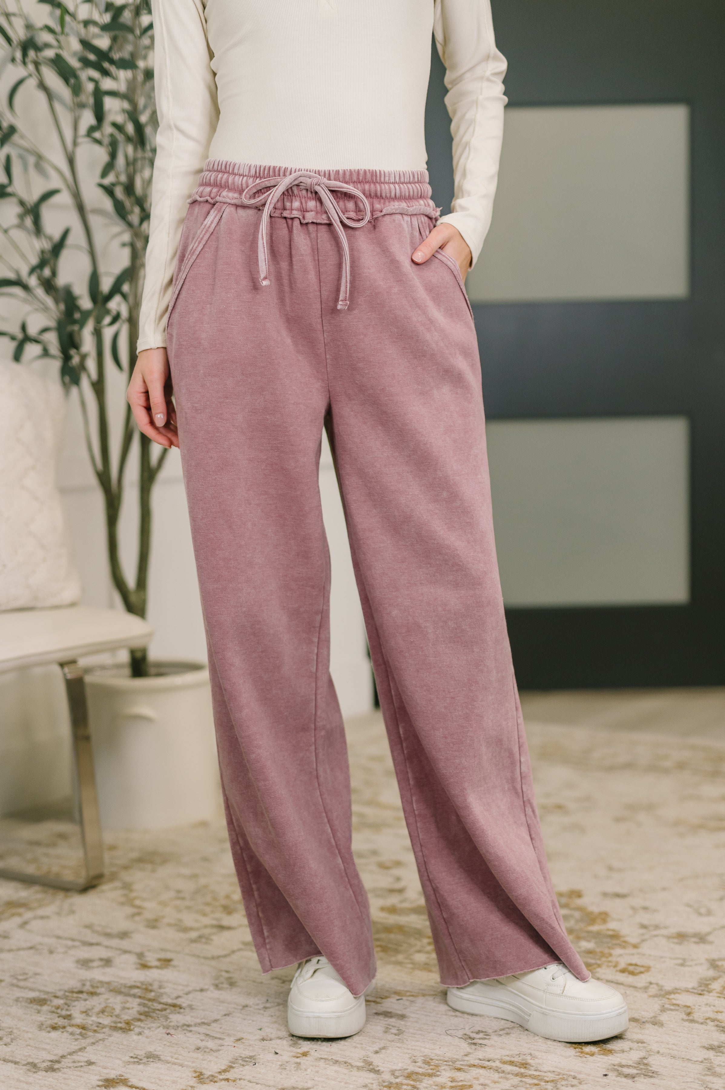 Woman wearing light rose high waist palazzo sweatpants with drawstring and side pockets paired with white sneakers indoors