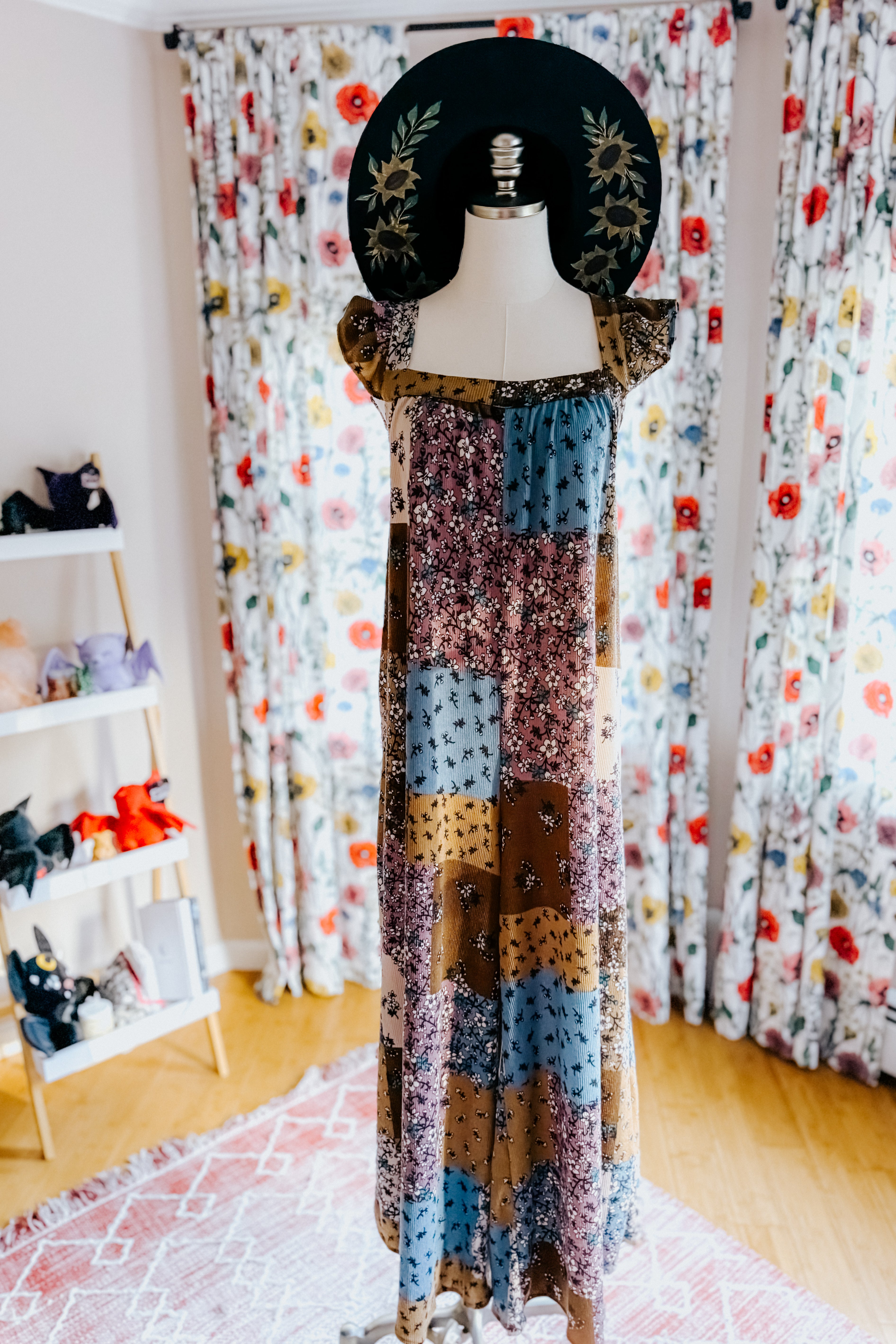 Long patchwork maxi dress in brown, blue, and cream knit fabric with a mix of floral prints and ruffle cap sleeves displayed on a mannequin.