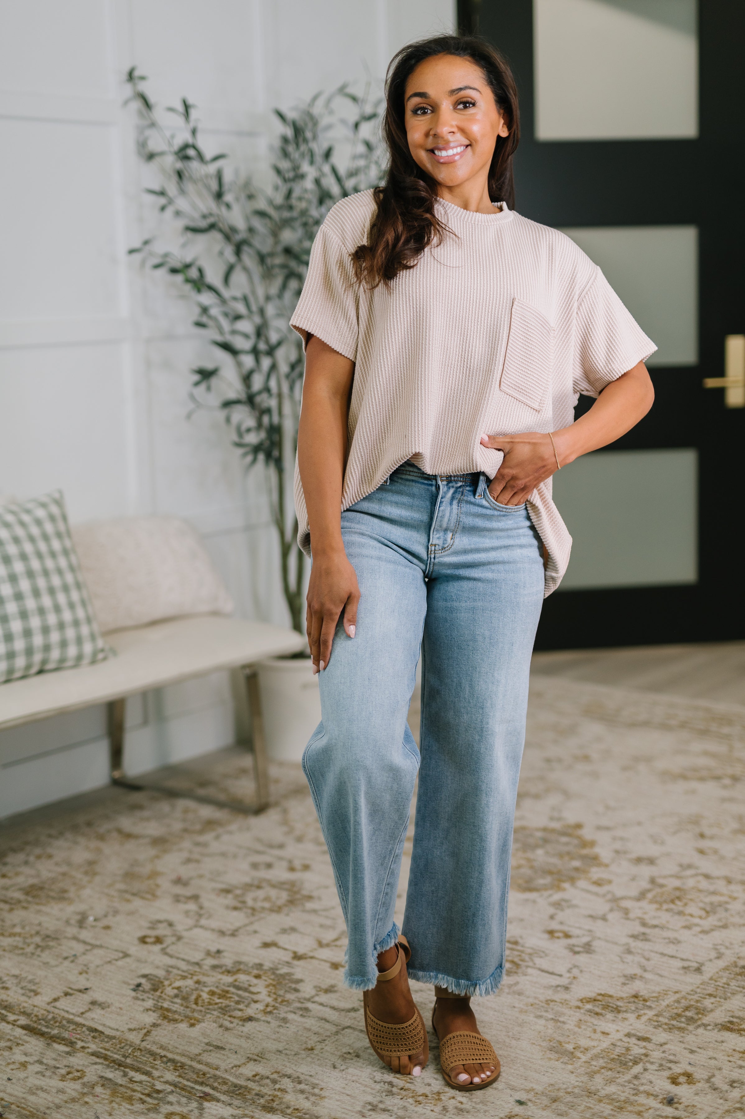Smiling woman wearing textured boxy ash mocha tee with front pocket and light washed wide-leg jeans indoors