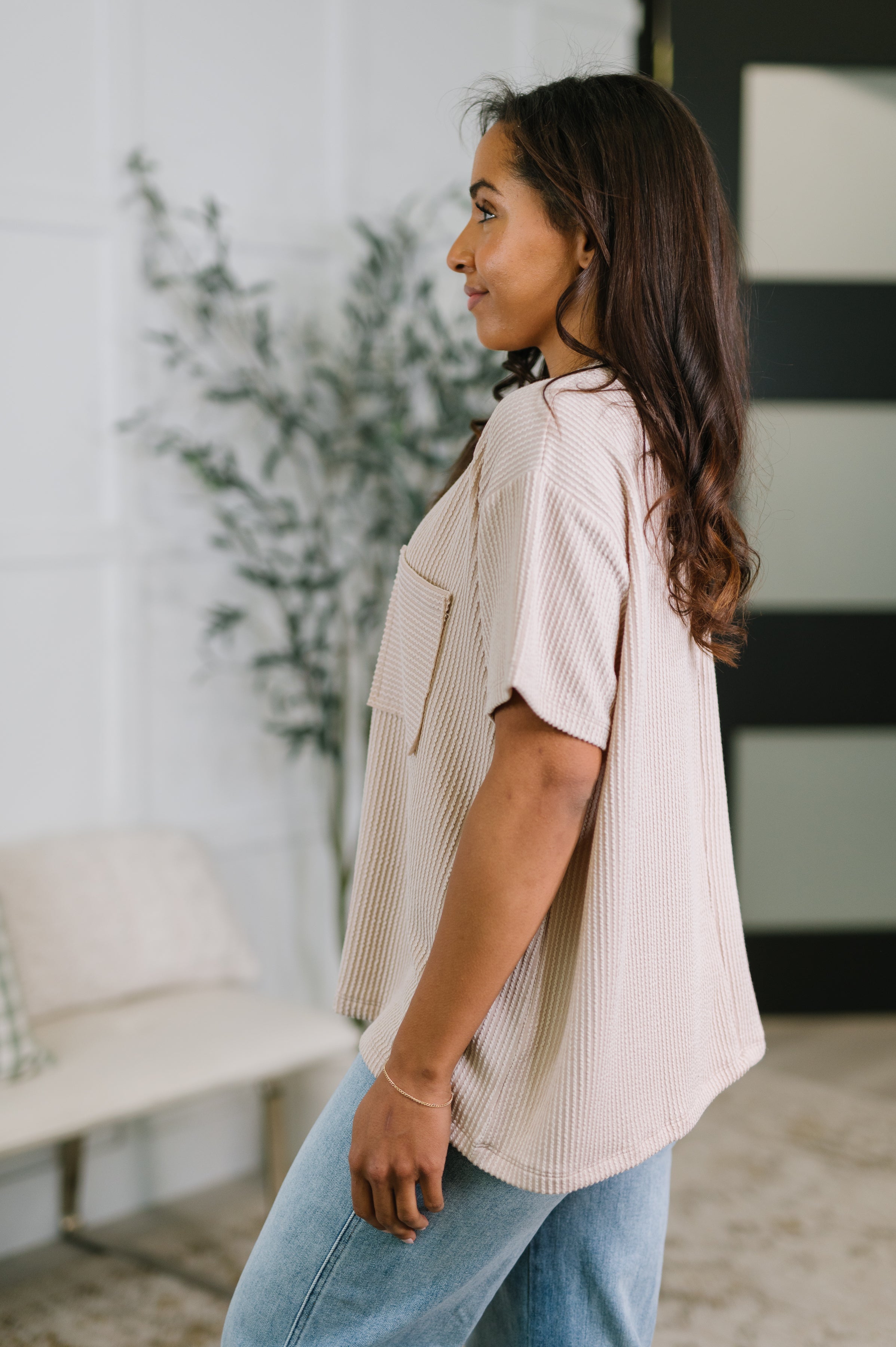 Side profile of woman wearing an ash mocha textured boxy tee with short sleeves and blue jeans indoors