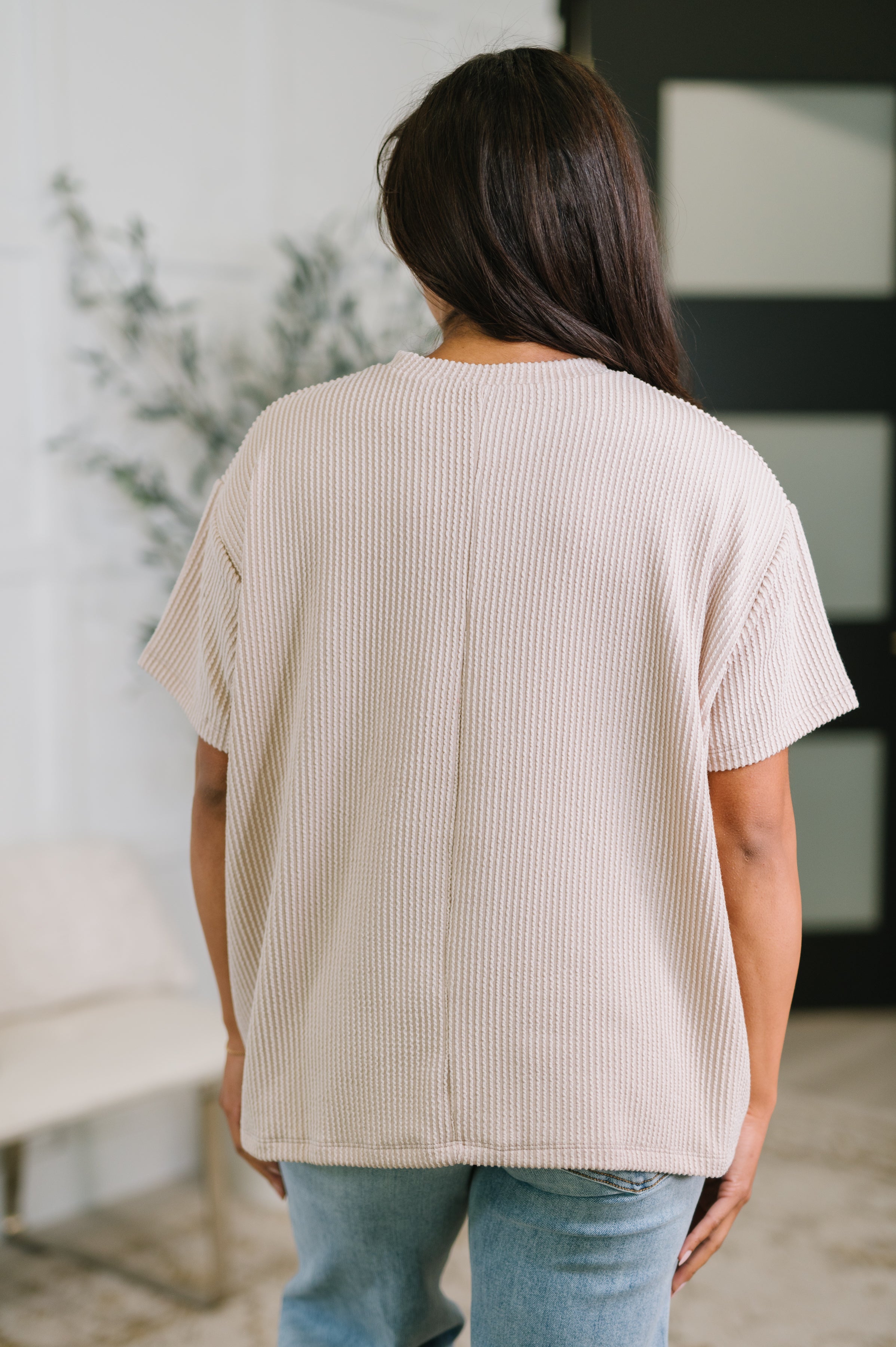 Back view of person wearing textured boxy tee in ash mocha with short sleeves and relaxed fit indoors