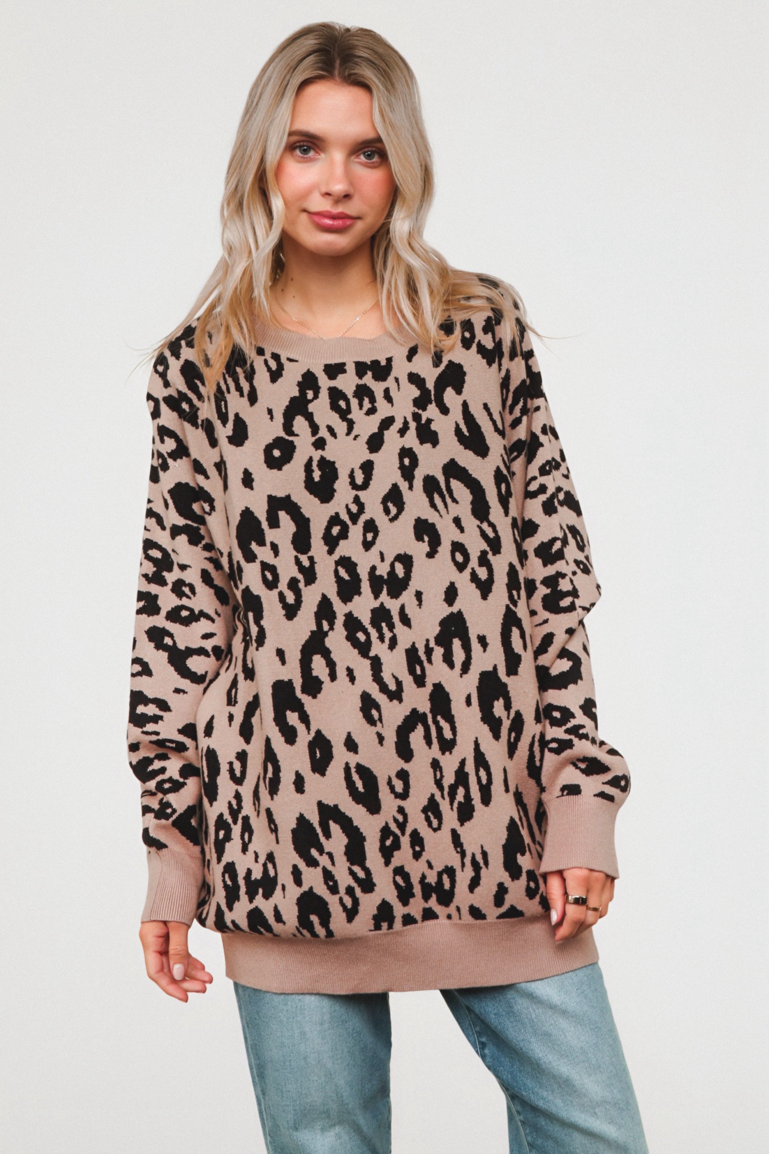 Woman wearing a relaxed mocha sweater with a bold black leopard print, paired with light wash jeans, standing against a plain background.