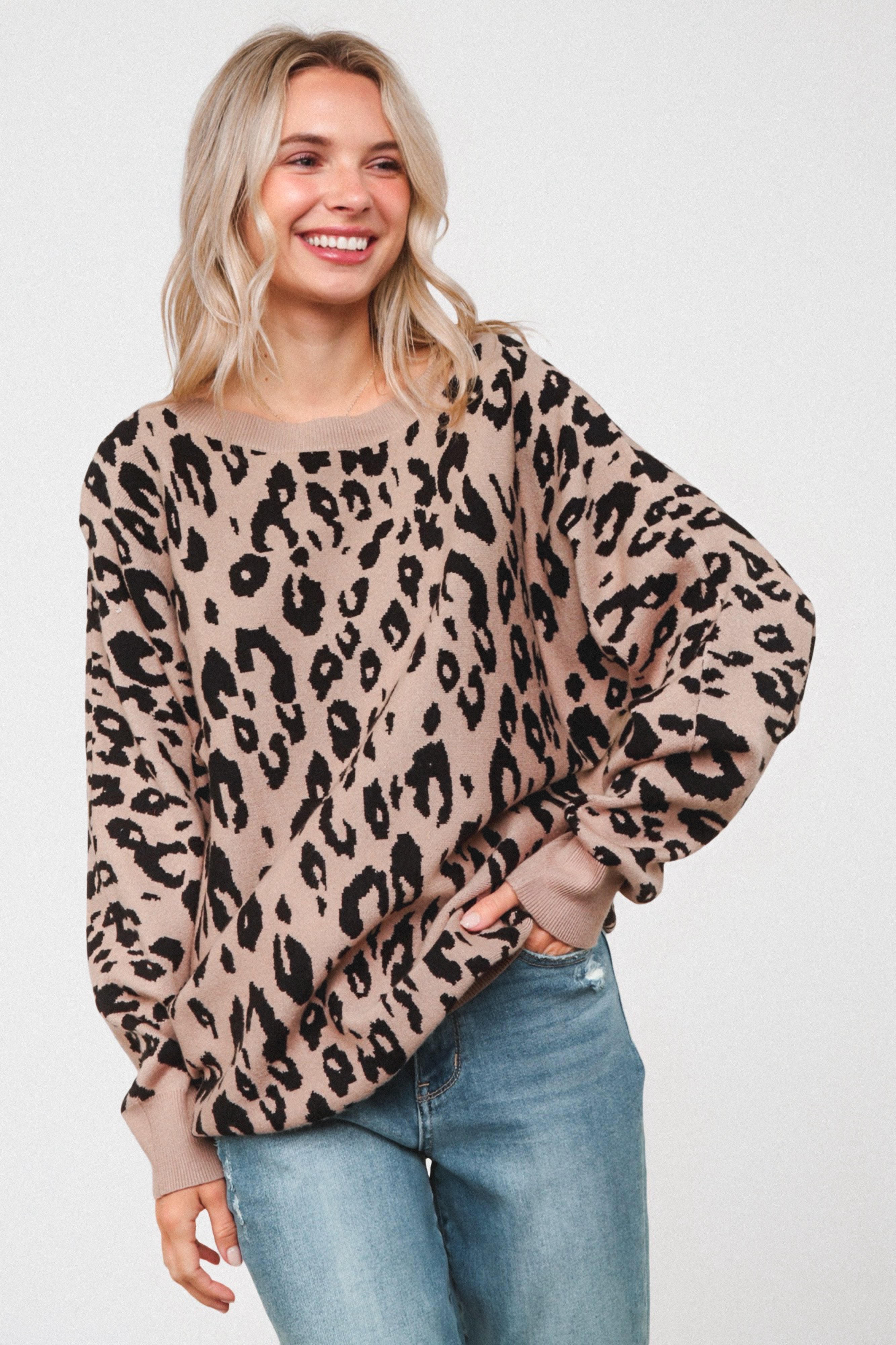 Smiling woman wearing a relaxed mocha sweater with a black leopard pattern, paired with medium wash blue jeans and posing with one hand in pocket.