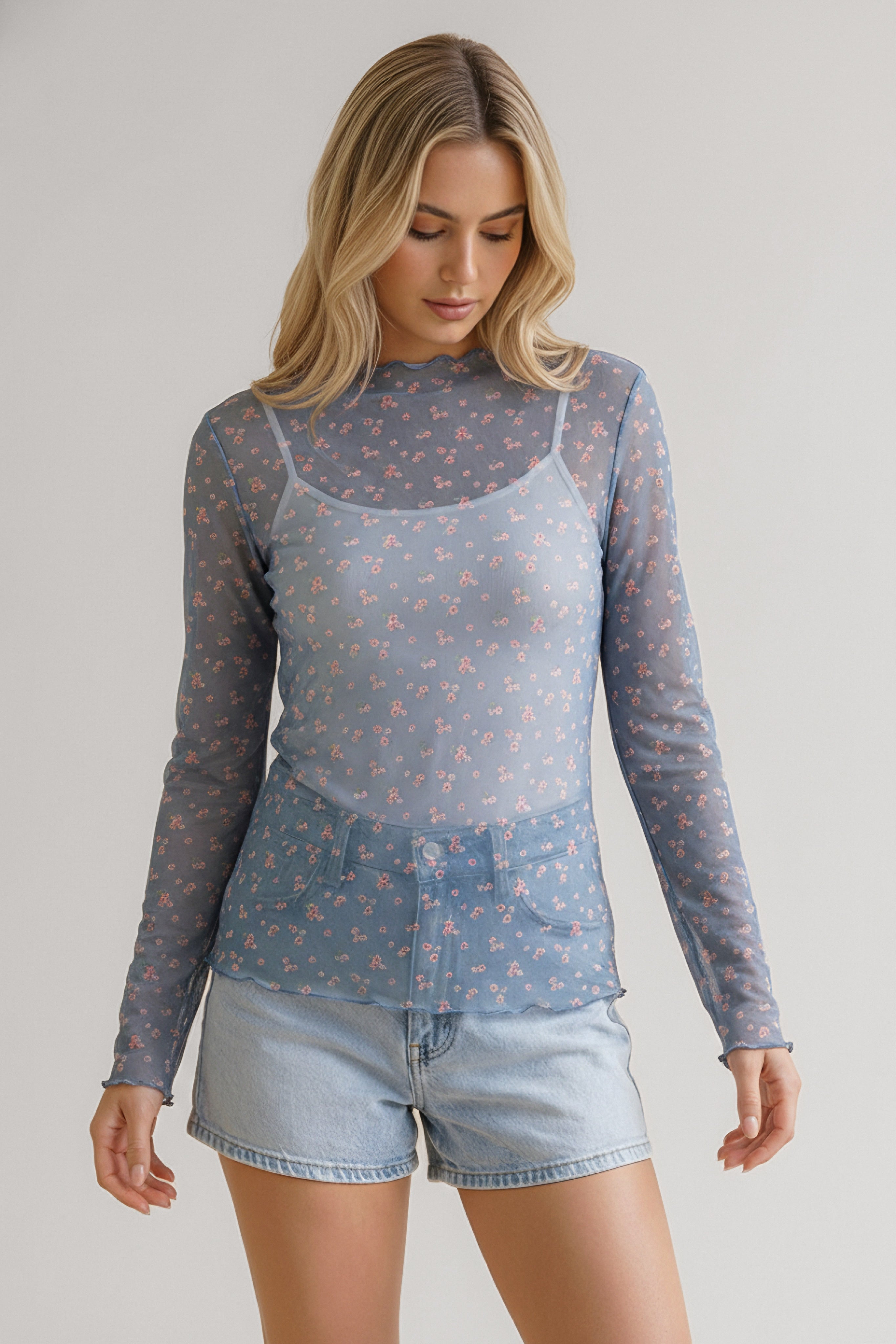 Woman wearing a sheer blue long-sleeve top with delicate pink floral print paired with light denim shorts
