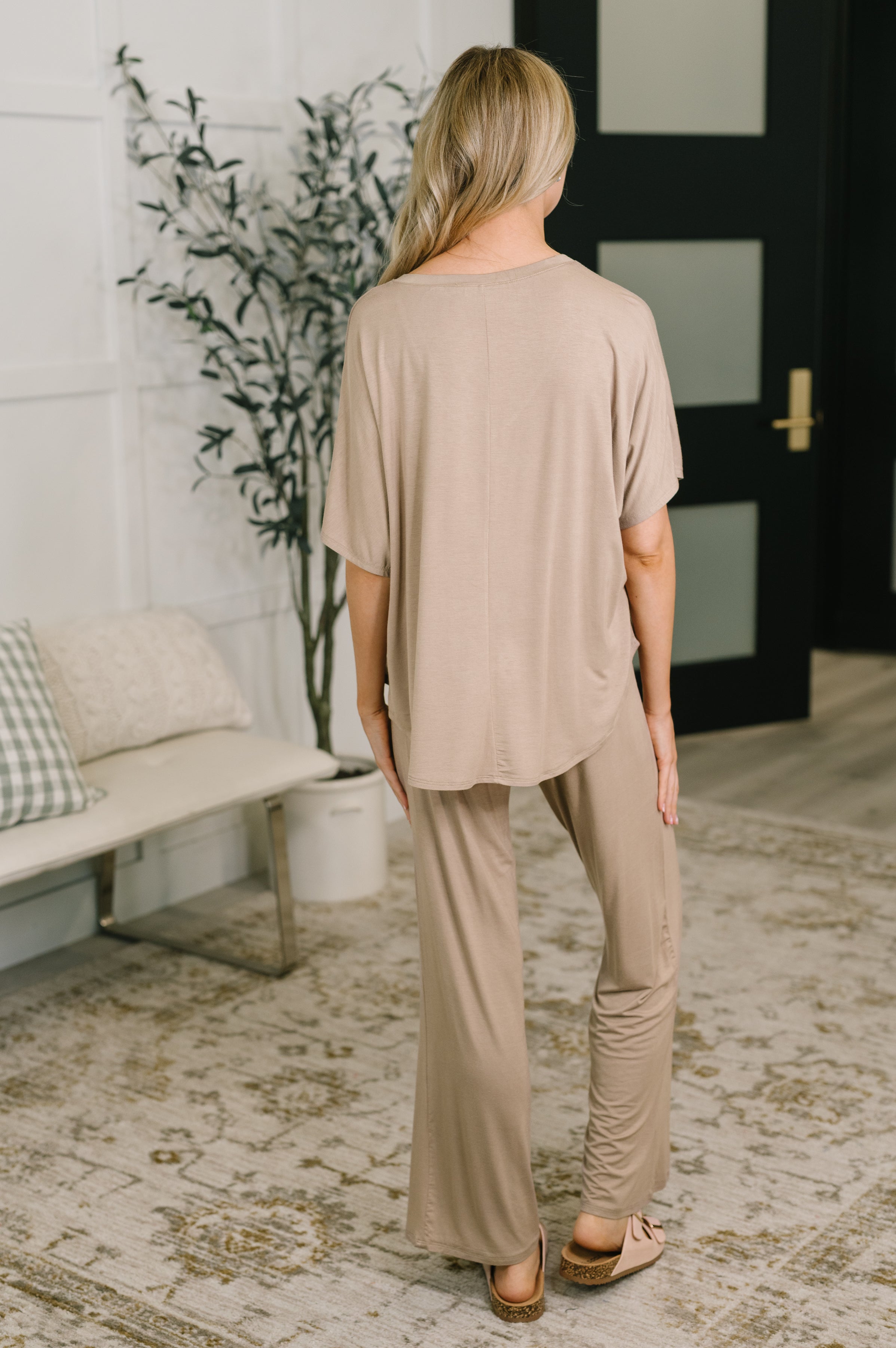 Woman seen from behind wearing beige lounge set with relaxed fit top and wide-leg pants indoors on patterned rug