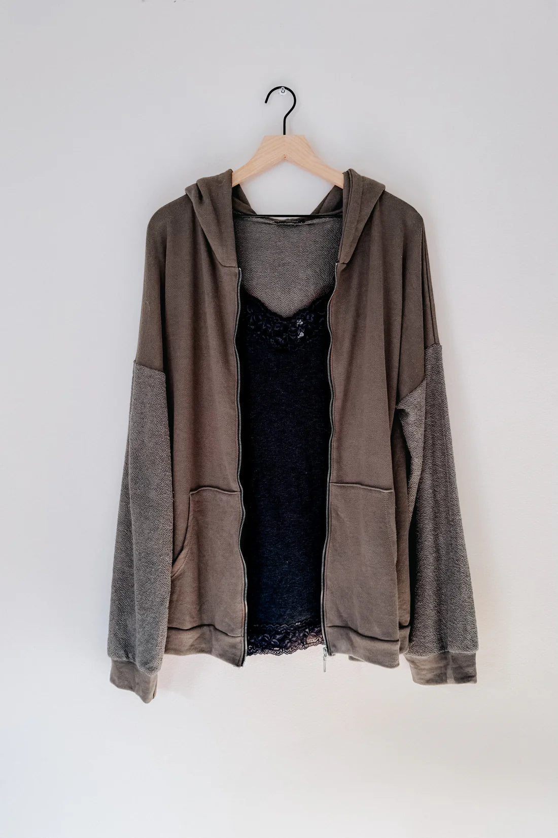 A brown zip up hoodie over a grey lace top hanging on a brown hanger against a white backdrop. 