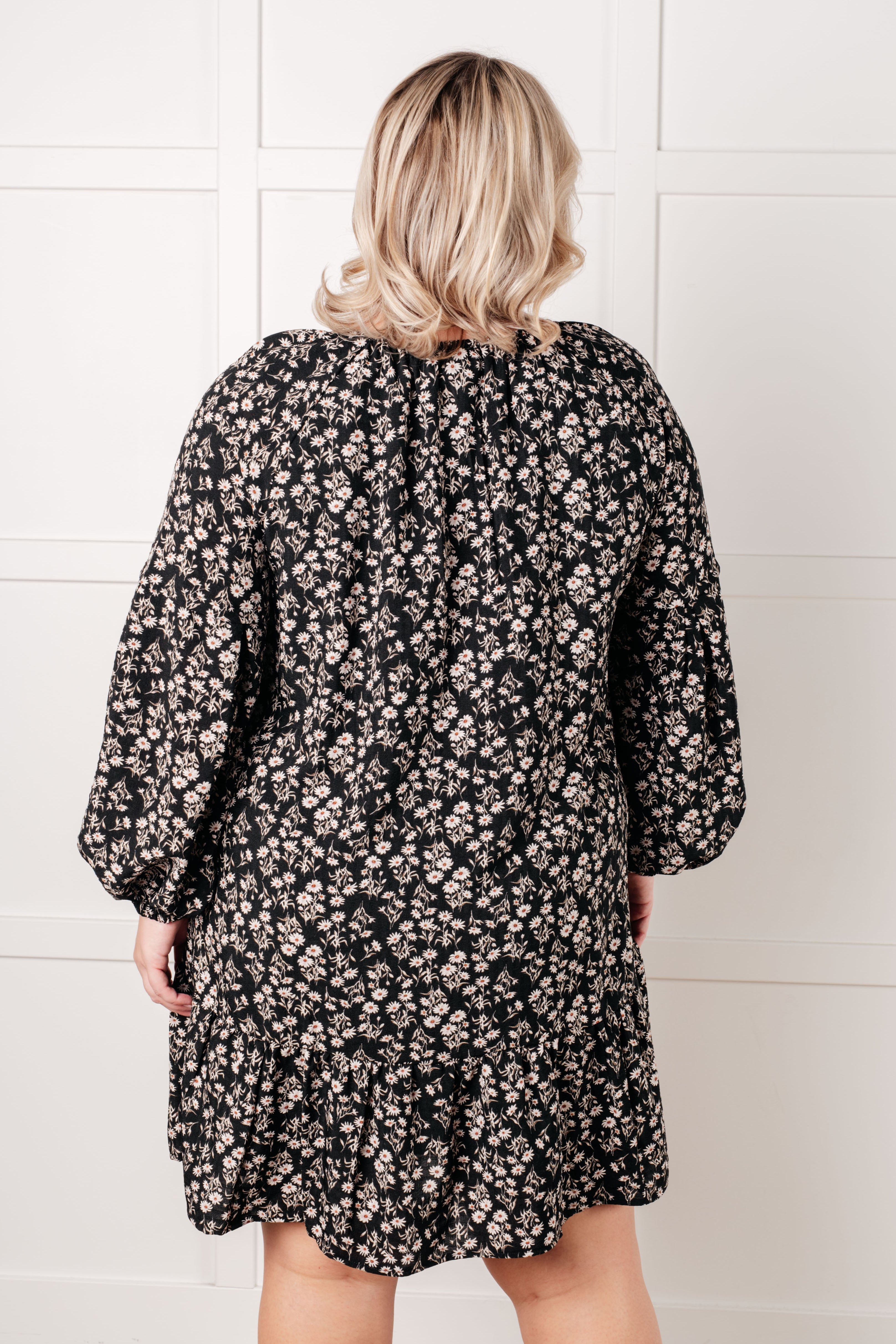 Plus size woman wearing a black floral dress with long sleeves and relaxed fit, shown from the back indoors