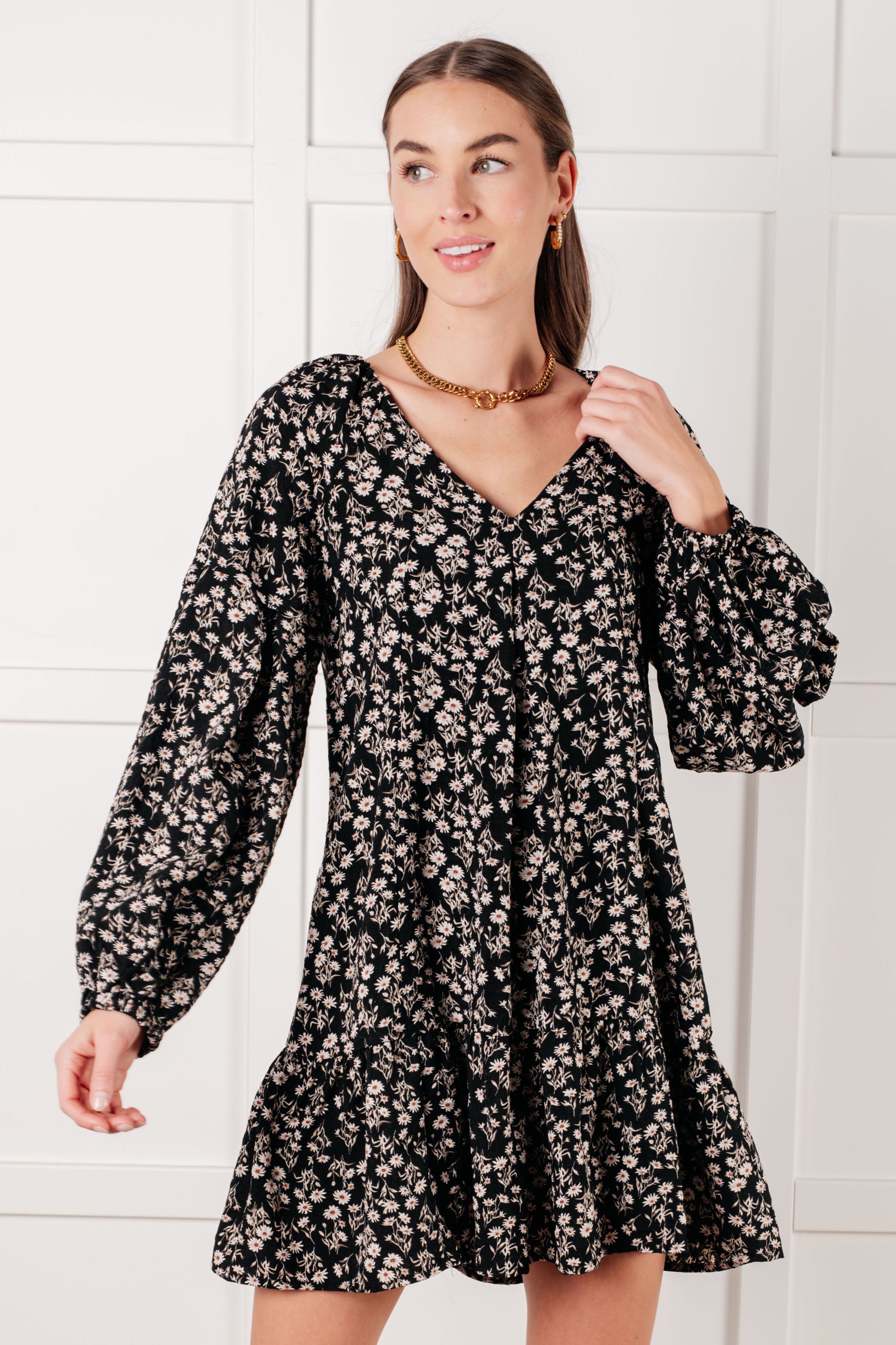 Woman wearing black floral dress with voluminous long sleeves and gold chain necklace posing indoors