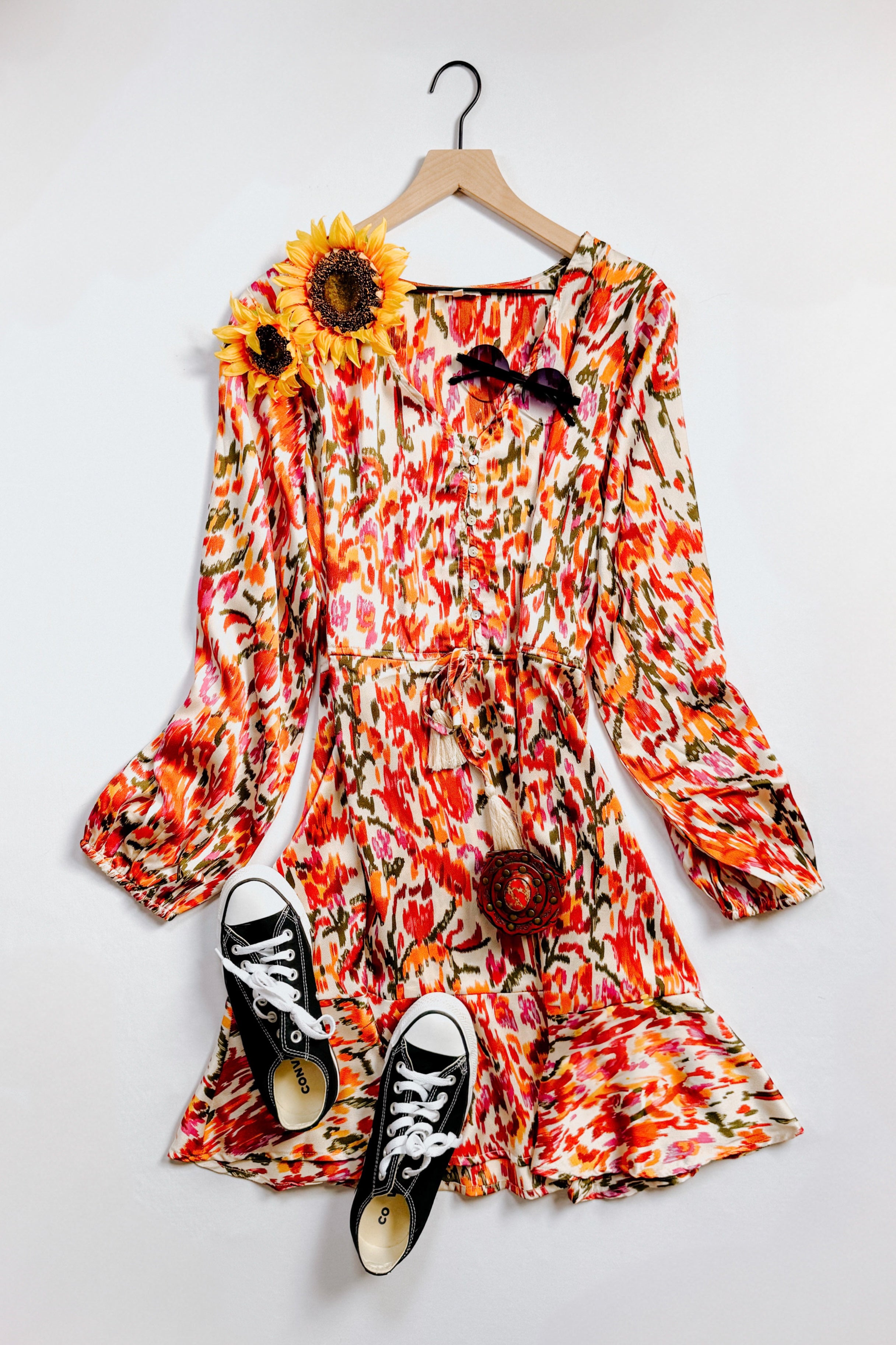 Orange patterned V-neck balloon sleeve dress with tie waist styled with black sneakers and sunglasses on white background
