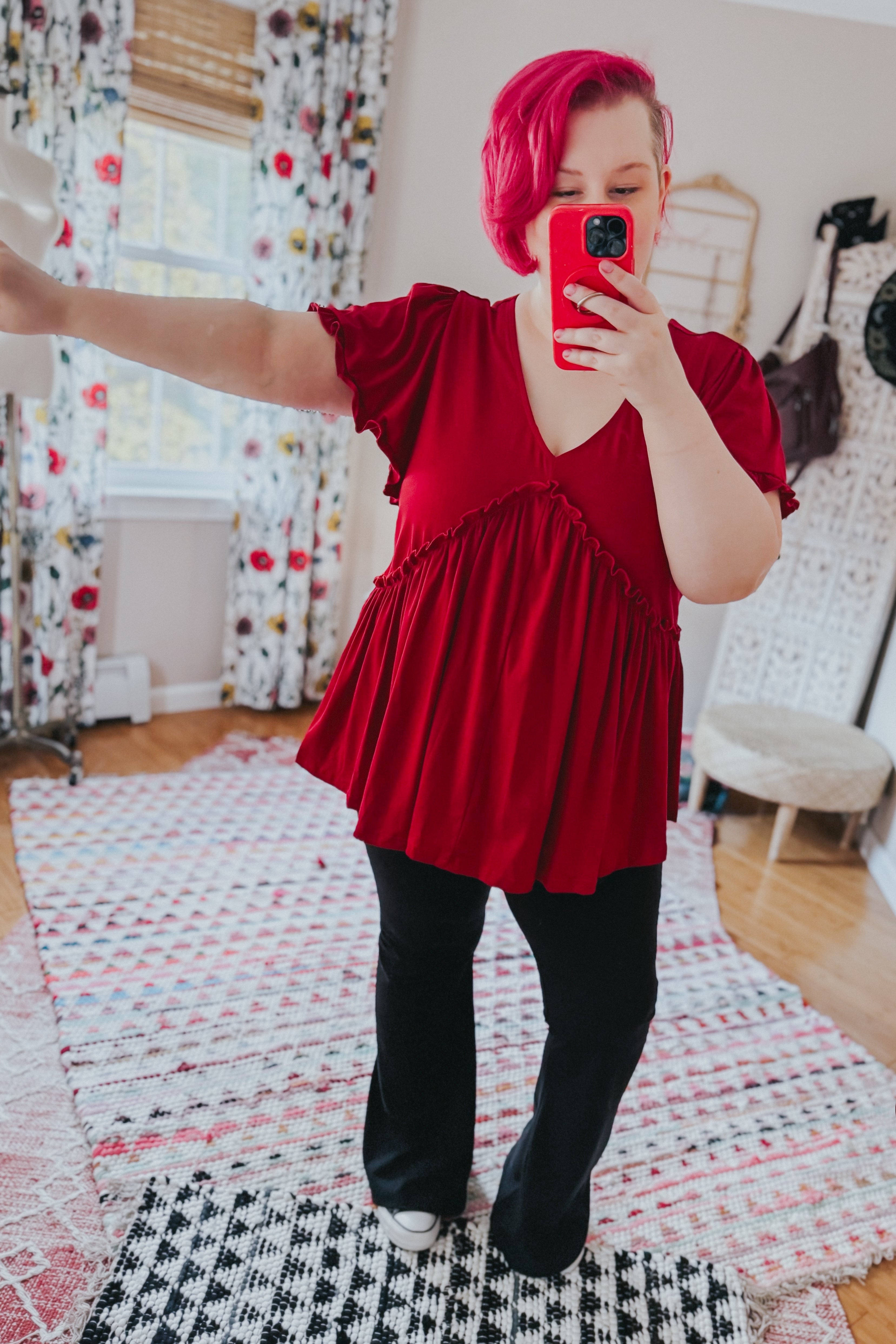 Woman with vibrant red hair wearing an eclectic red V-neck top with ruffle details and flutter sleeves paired with black pants