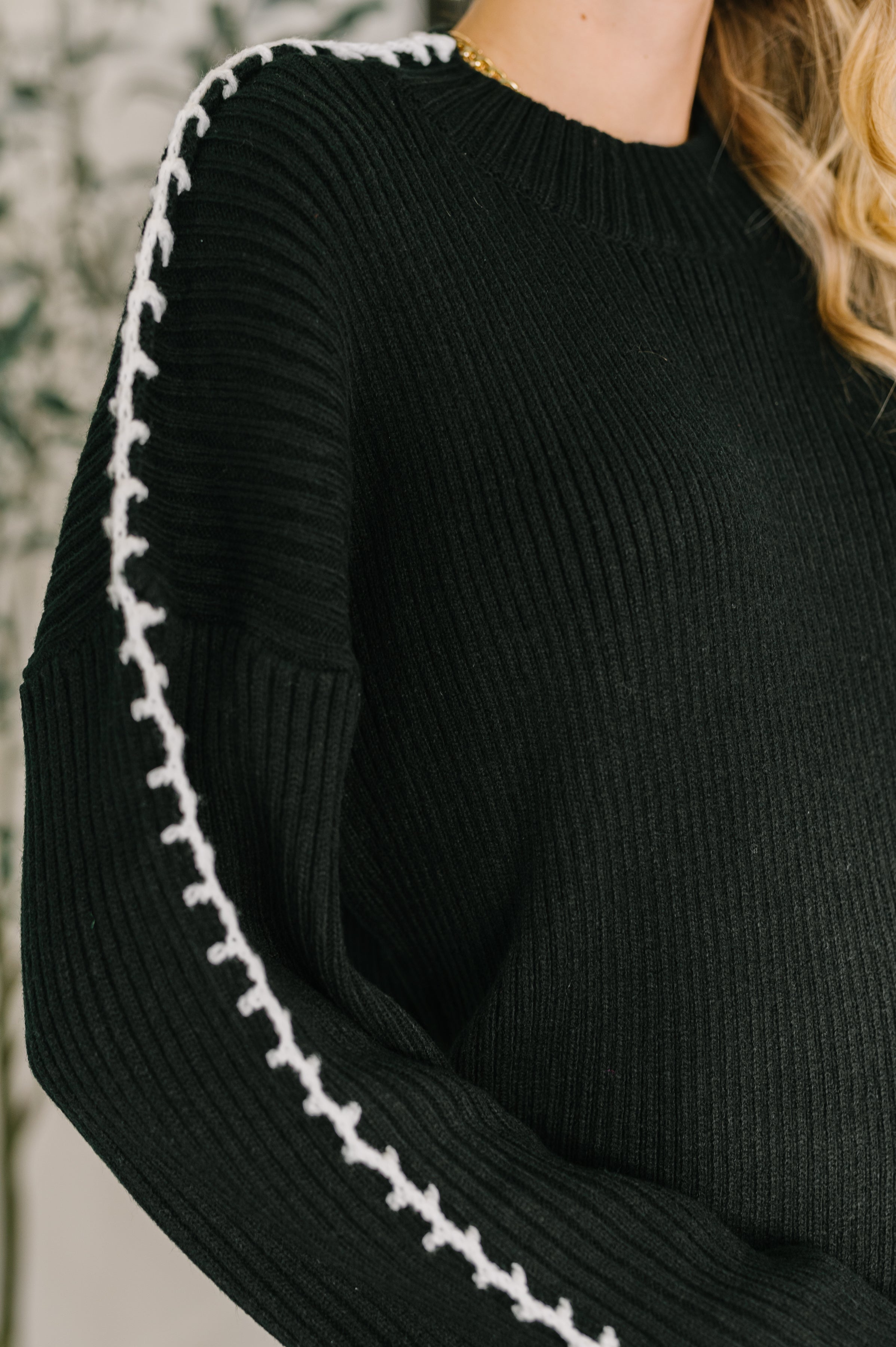 Close-up of black ribbed knit pullover with white stitch detailing along the sleeve for a free-spirited look
