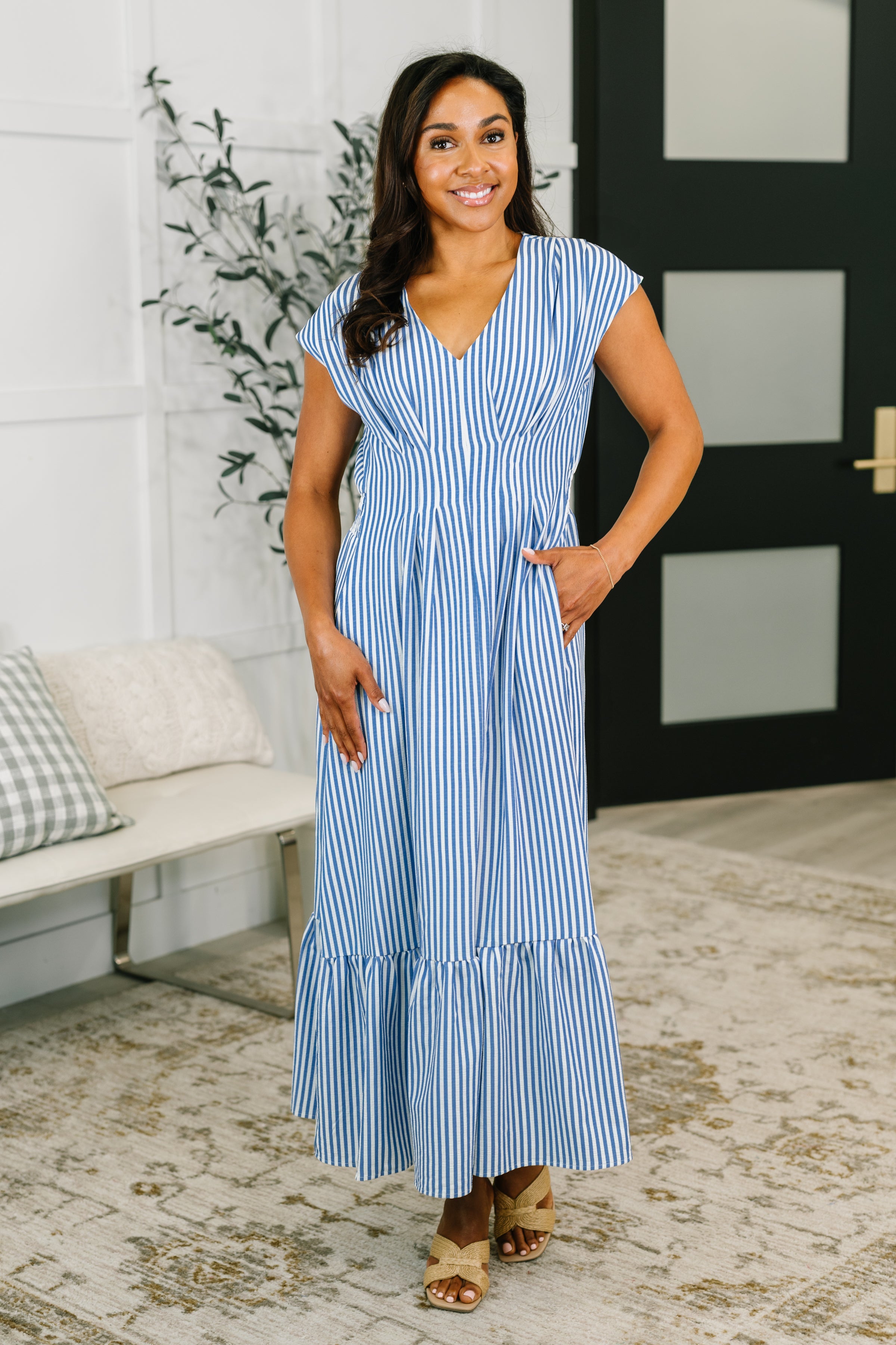Woman wearing a blue and white striped smock waist maxi dress with cap sleeves in an eclectic indoor setting