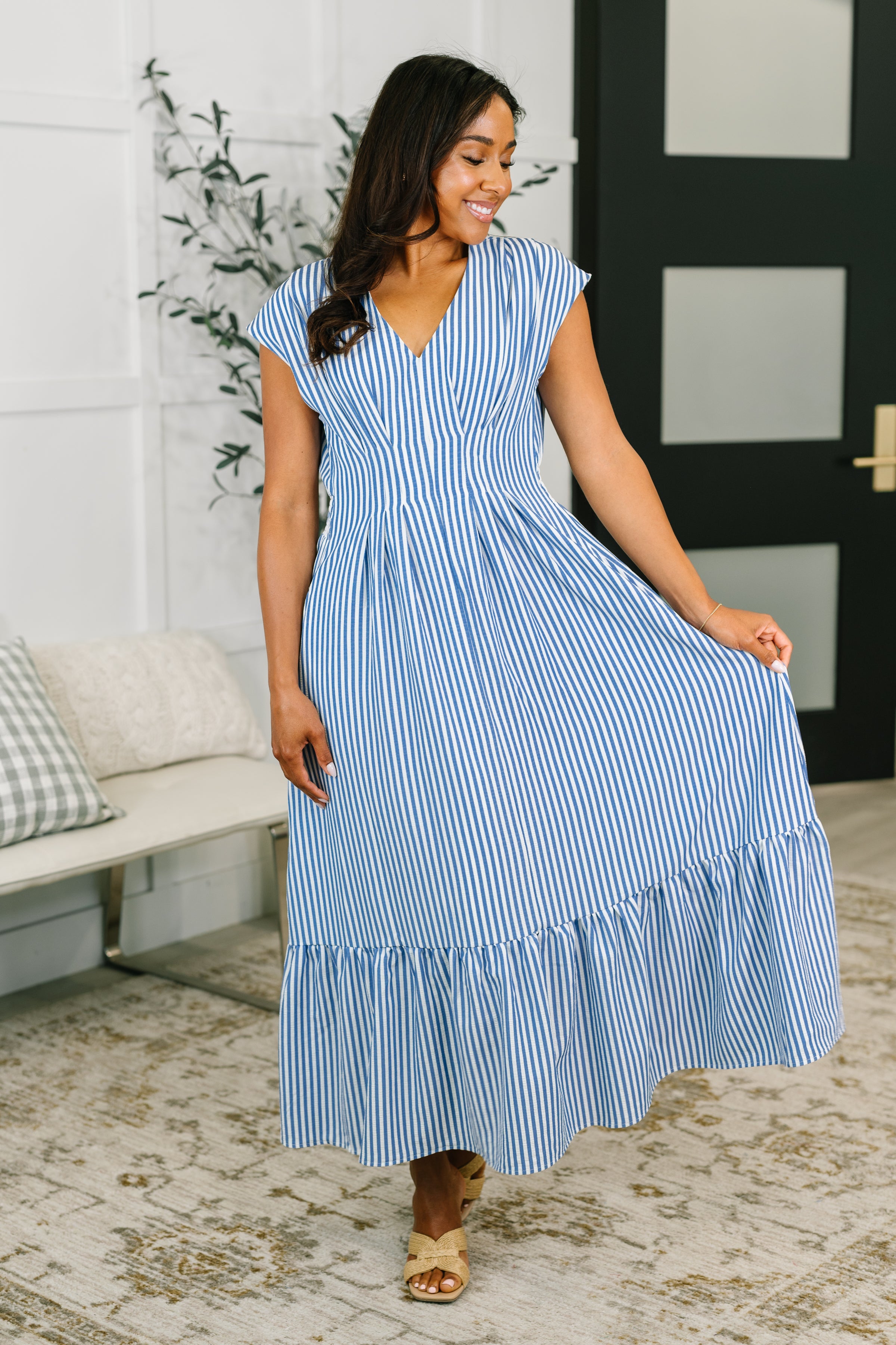 Woman wearing blue and white striped pleated dress with cap sleeves in a bright eclectic free-spirited indoor space