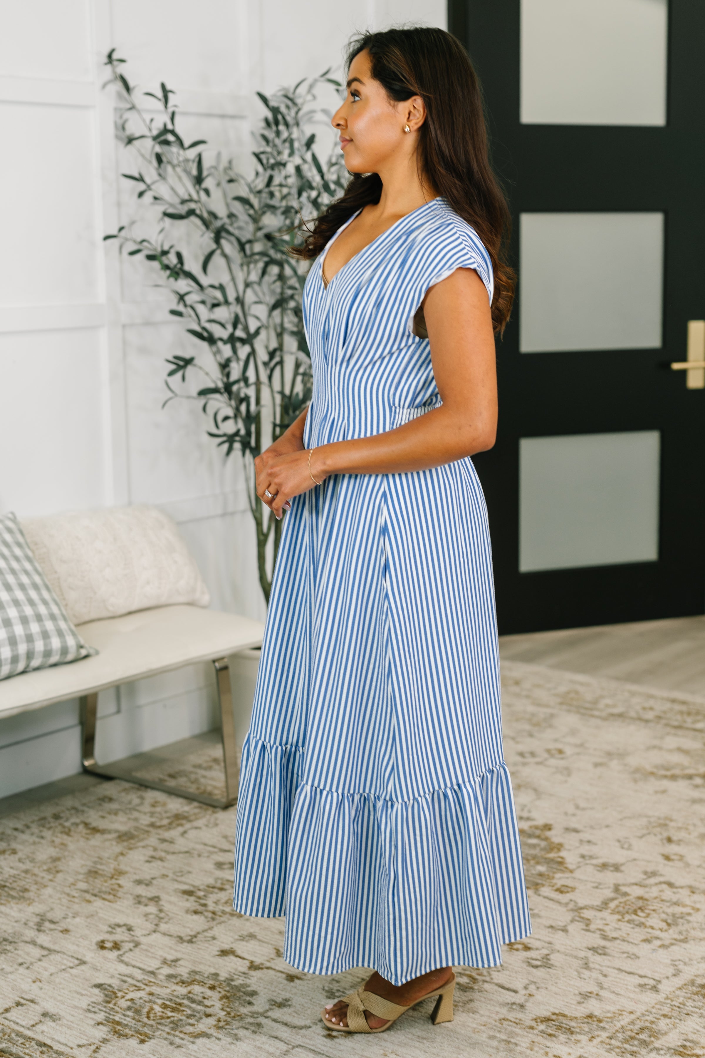 Woman wearing a blue striped pleated maxi dress with cap sleeves in a bright, eclectic indoor setting