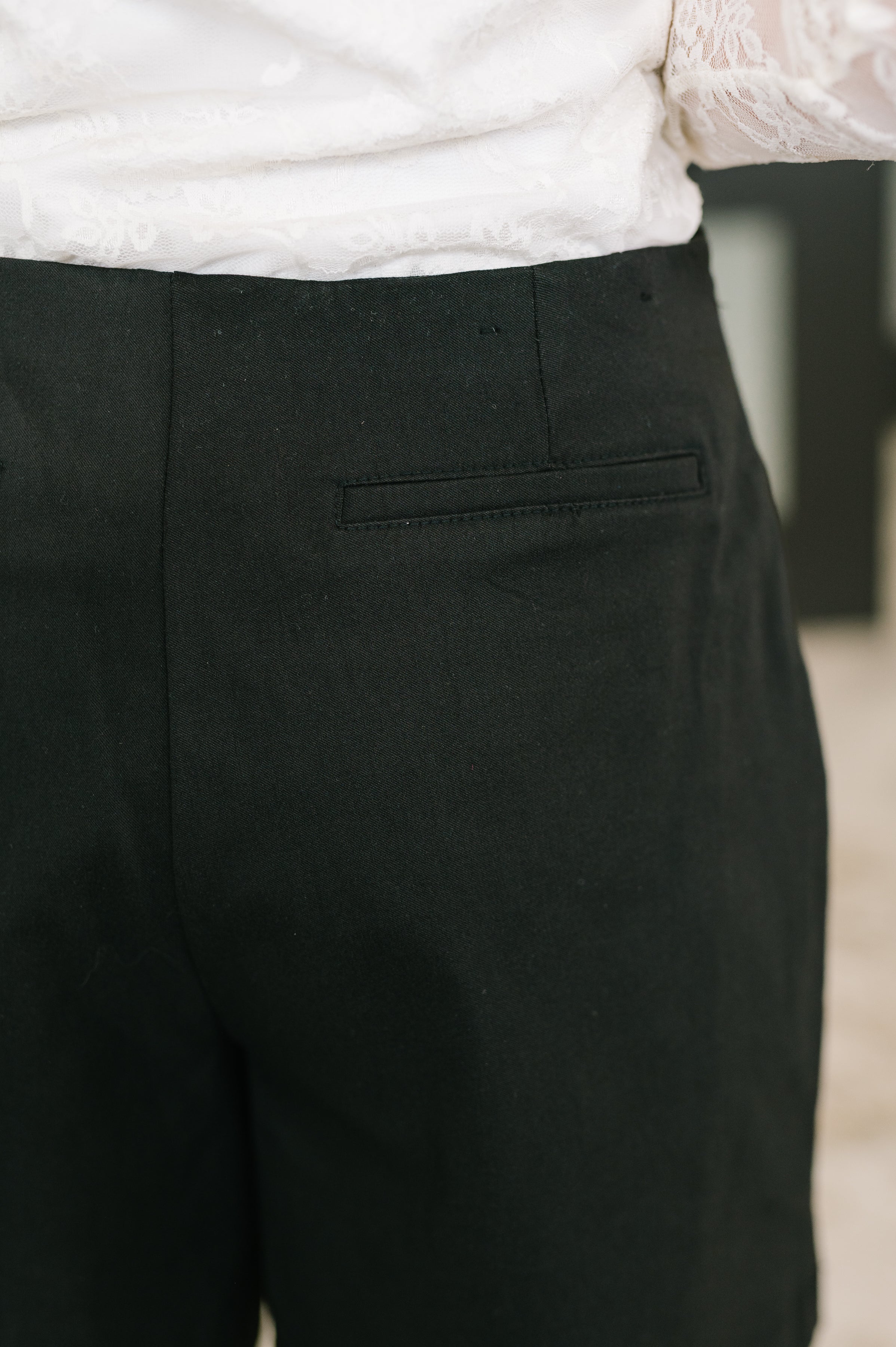 Close-up of black faux wrap skort back with welt pocket detail paired with white lace top in soft indoor light