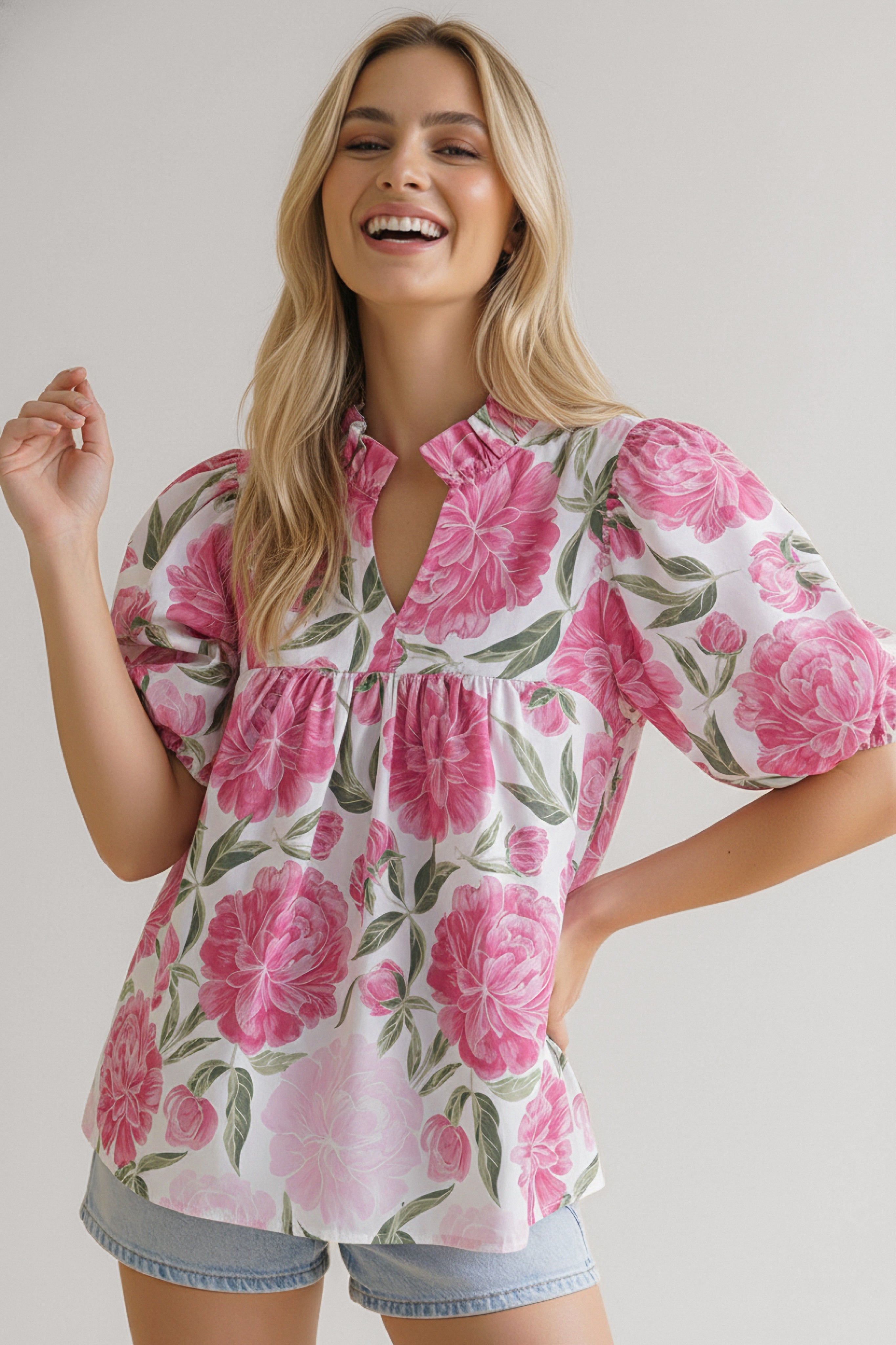 Smiling woman wearing a pink floral puff-sleeve blouse with a mandarin collar paired with light denim shorts