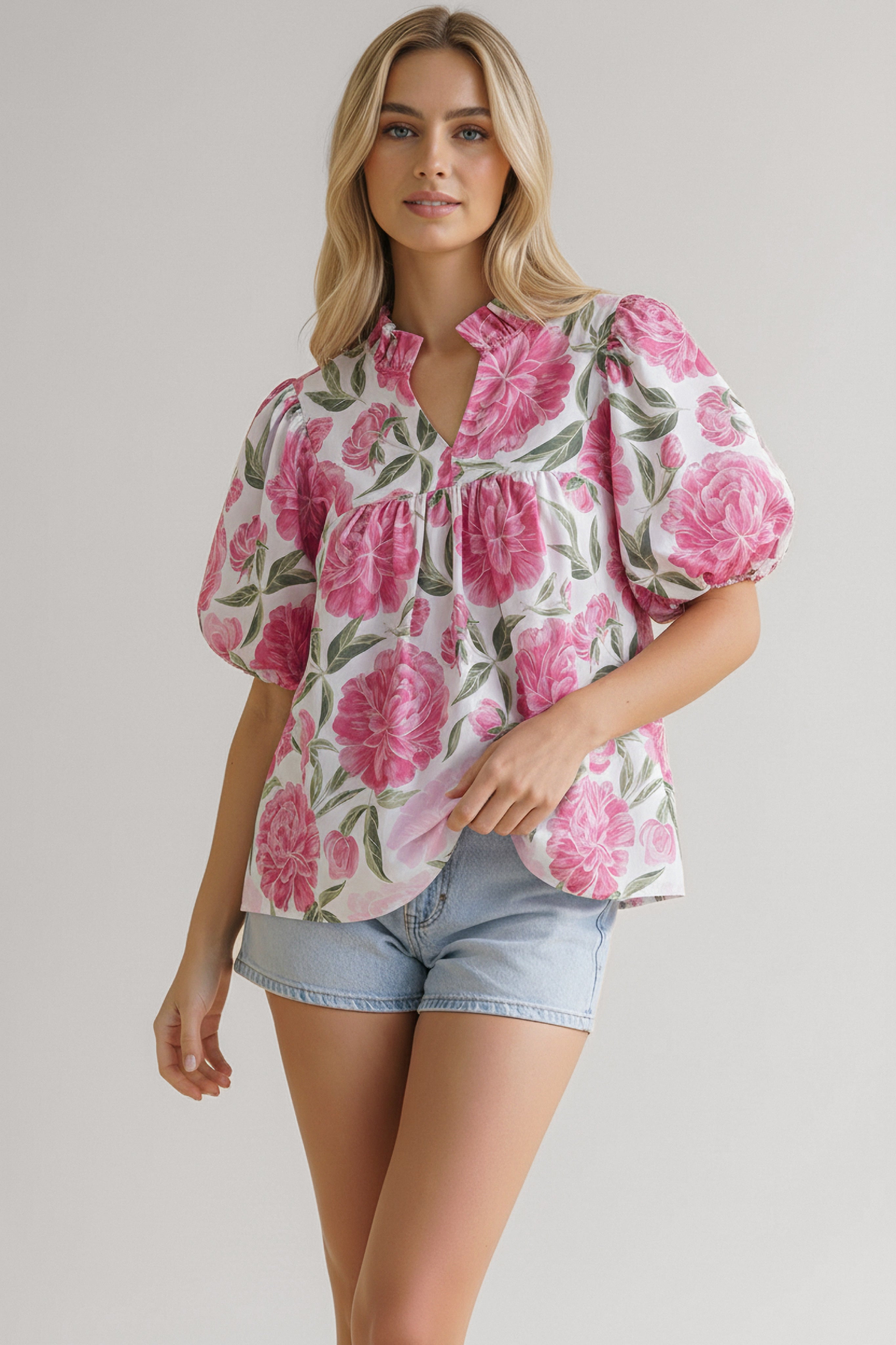 Woman wearing a pink floral print blouse with puff sleeves and ruffle neckline paired with light denim shorts
