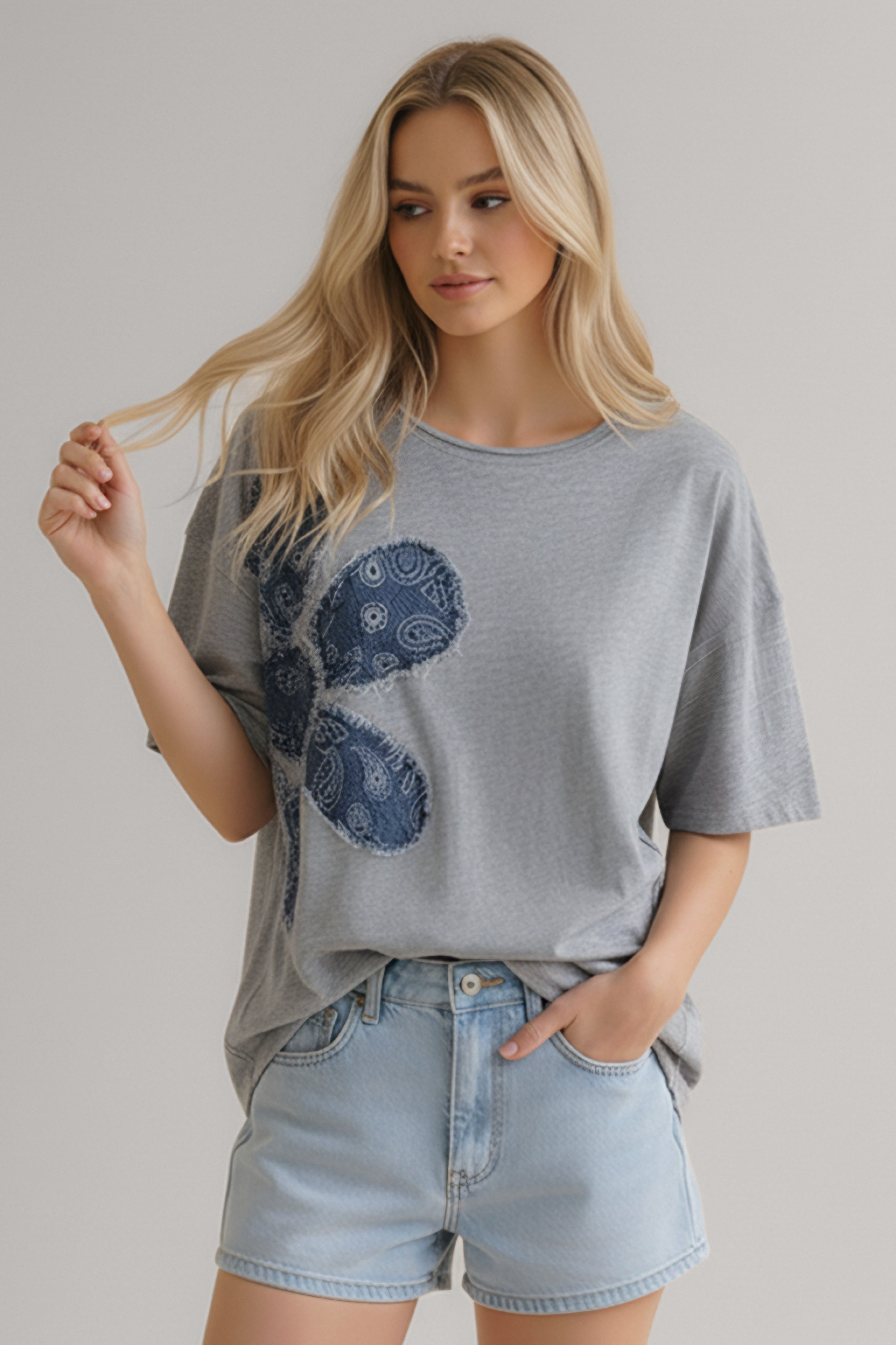 Woman wearing a heather grey T-shirt with a large navy blue paisley floral appliqué and light denim shorts