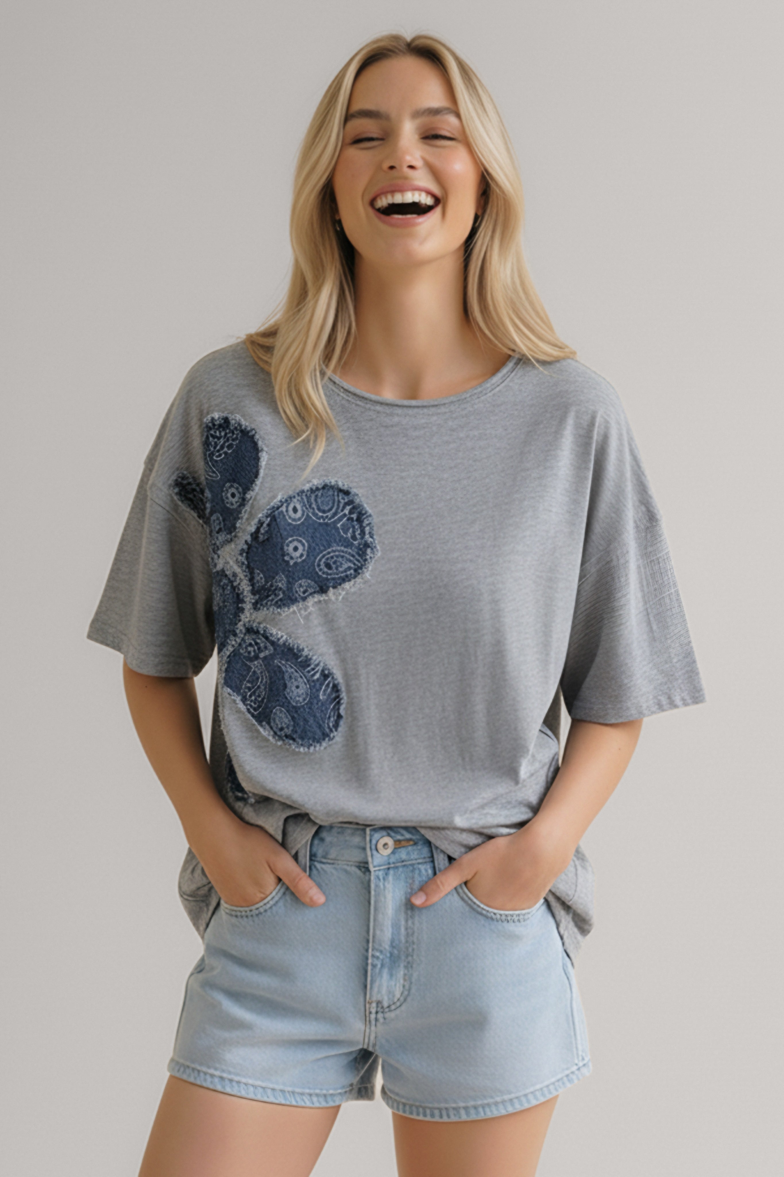 Woman wearing a heather grey T-shirt with a large navy floral appliqué paired with light denim shorts