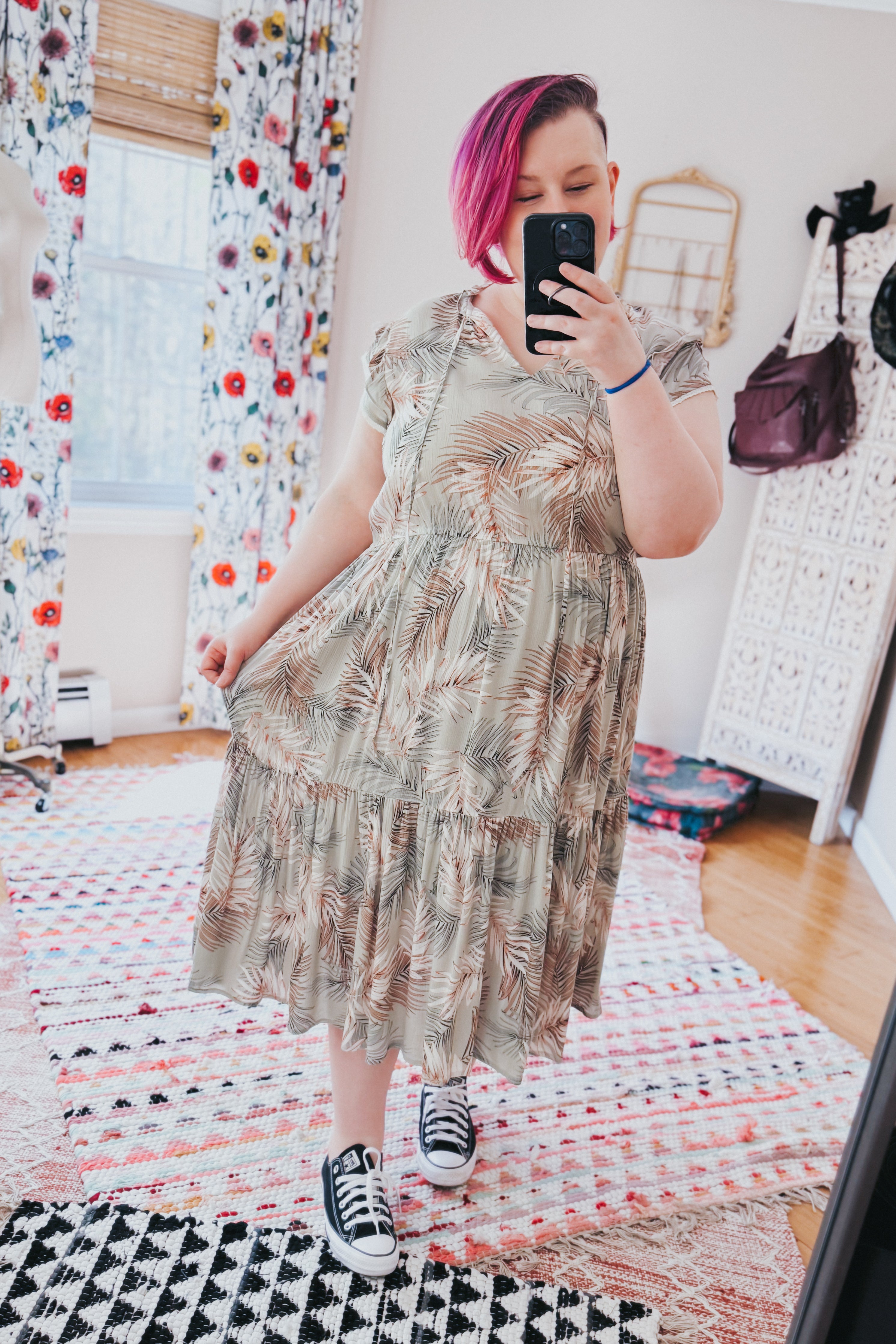 Woman with pink hair wearing green Palms & Paradise tiered midi dress with palm leaf pattern and black sneakers indoors