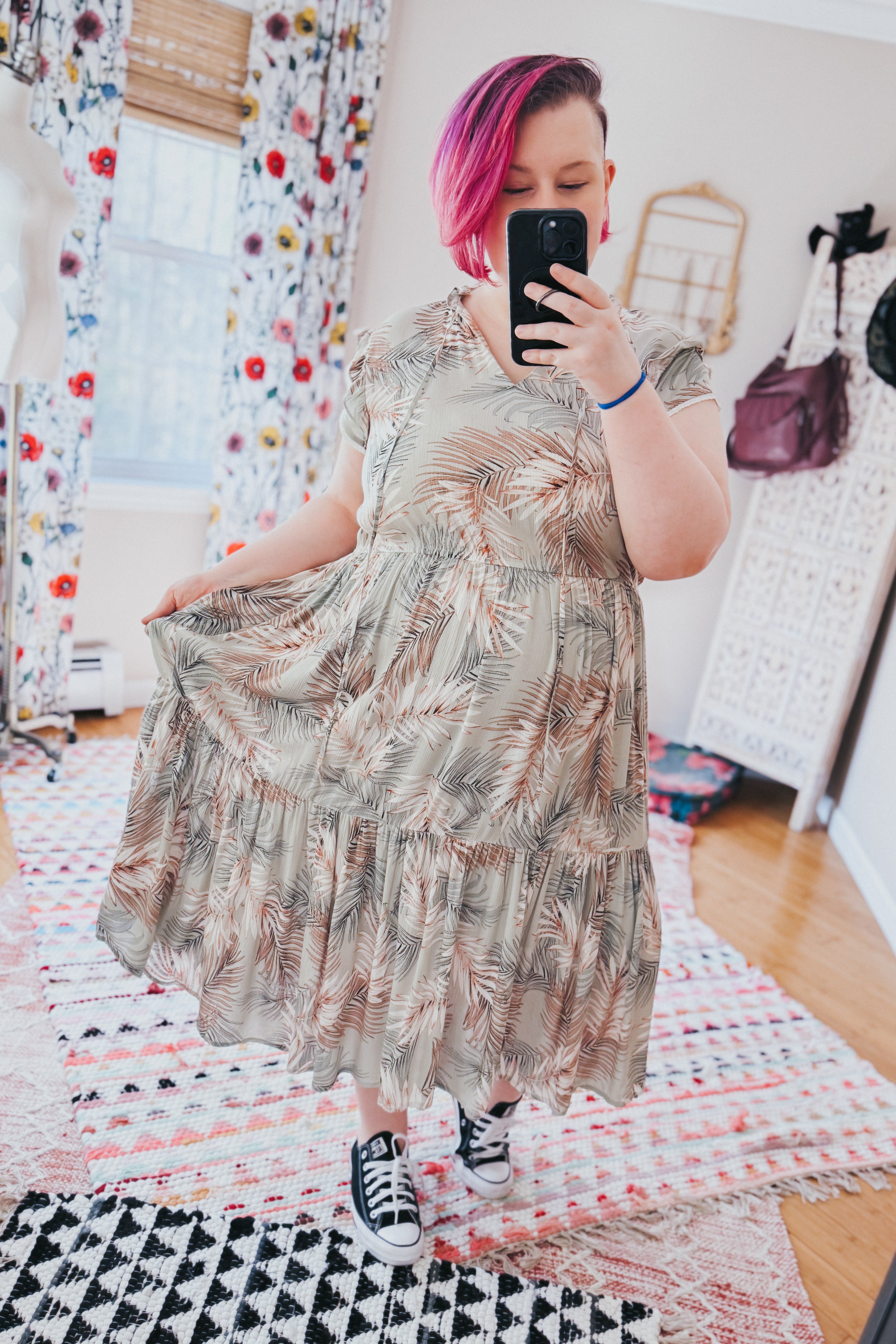 Woman with pink hair wearing green palm print tiered midi dress paired with black sneakers in cozy room setting