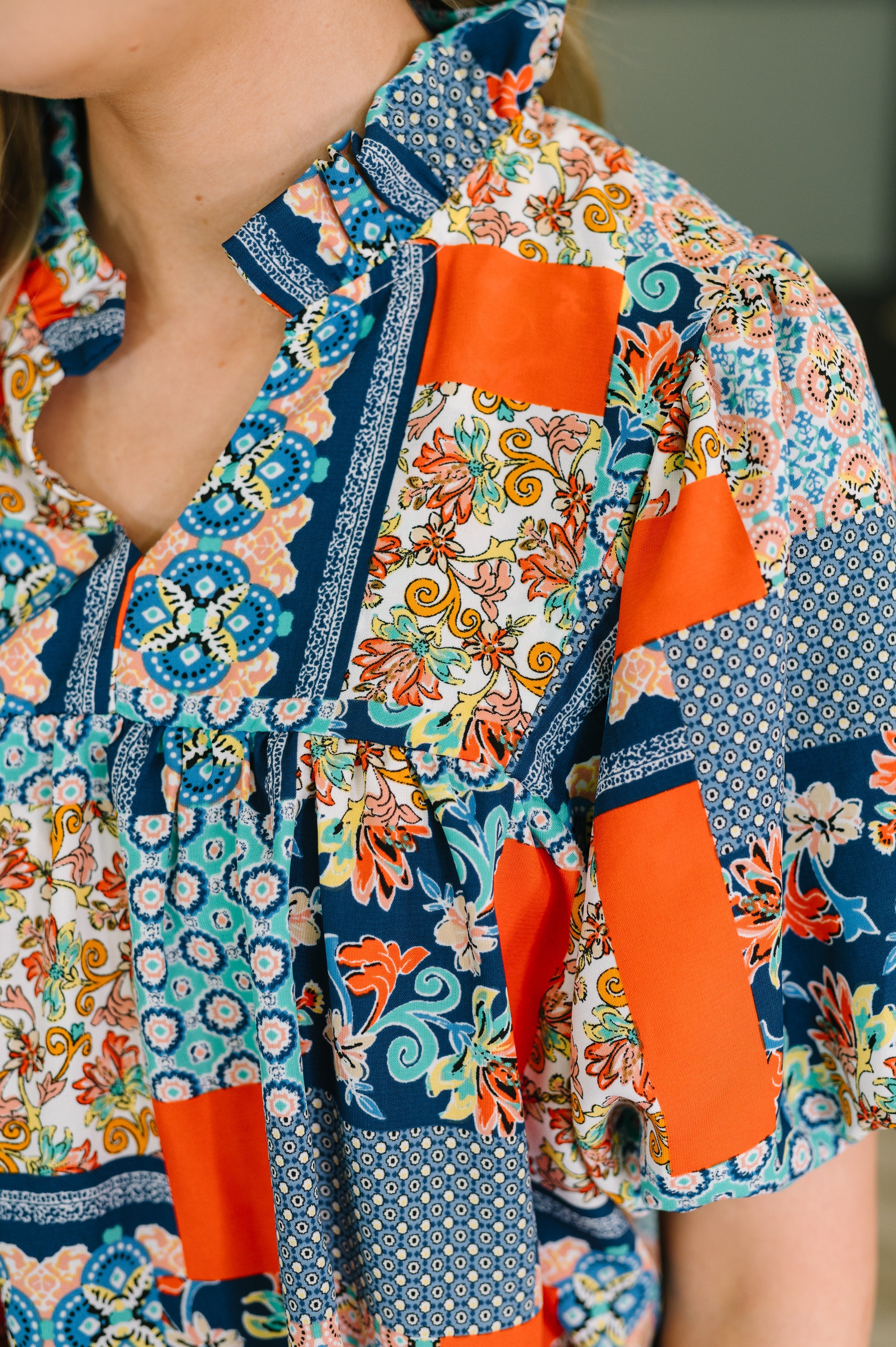Woman wearing a blue patchwork blouse with a ruffled split neckline and statement puff sleeves indoors
