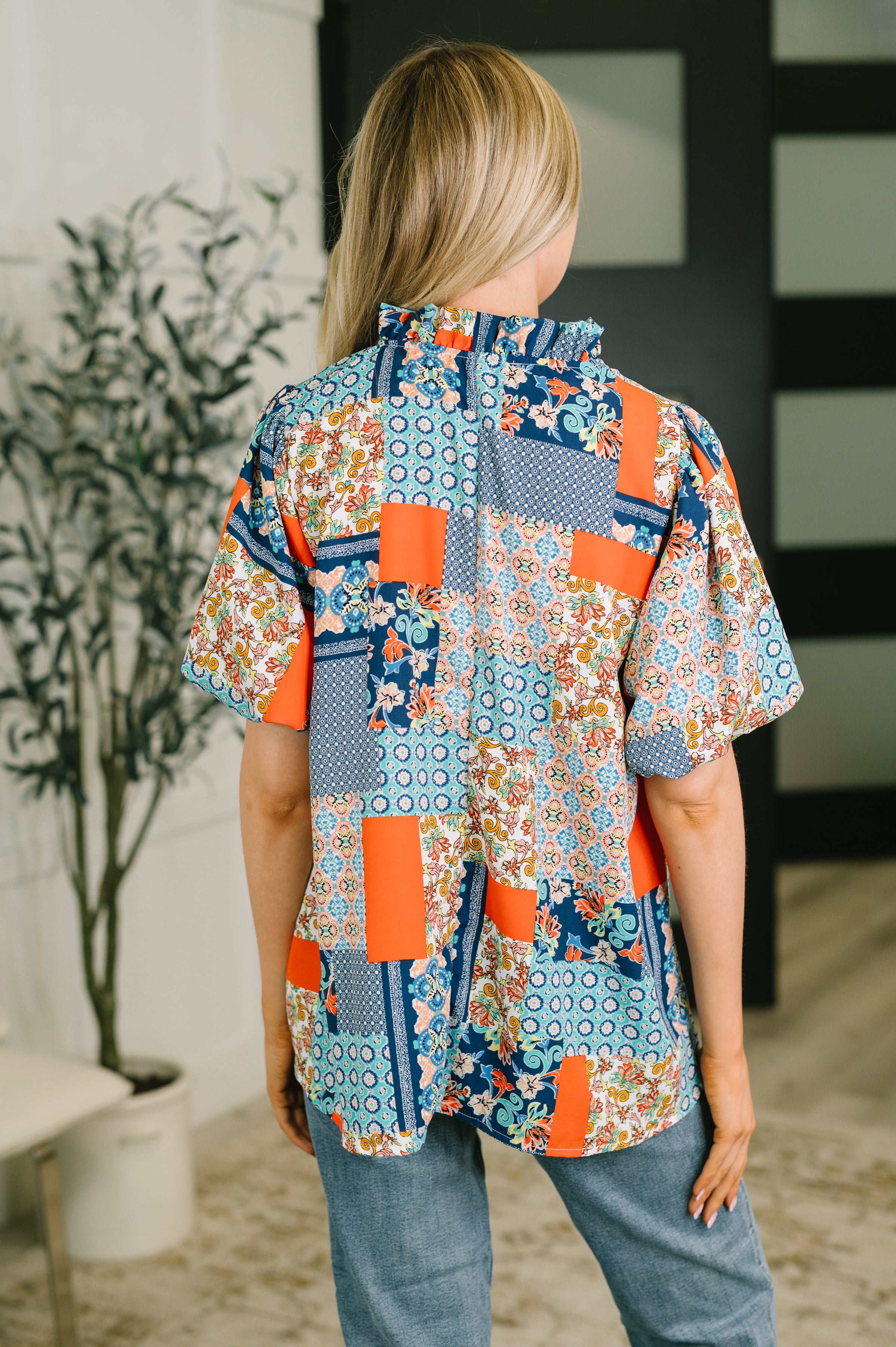 Back view of woman wearing a blue patchwork blouse with short sleeves and jeans indoors
