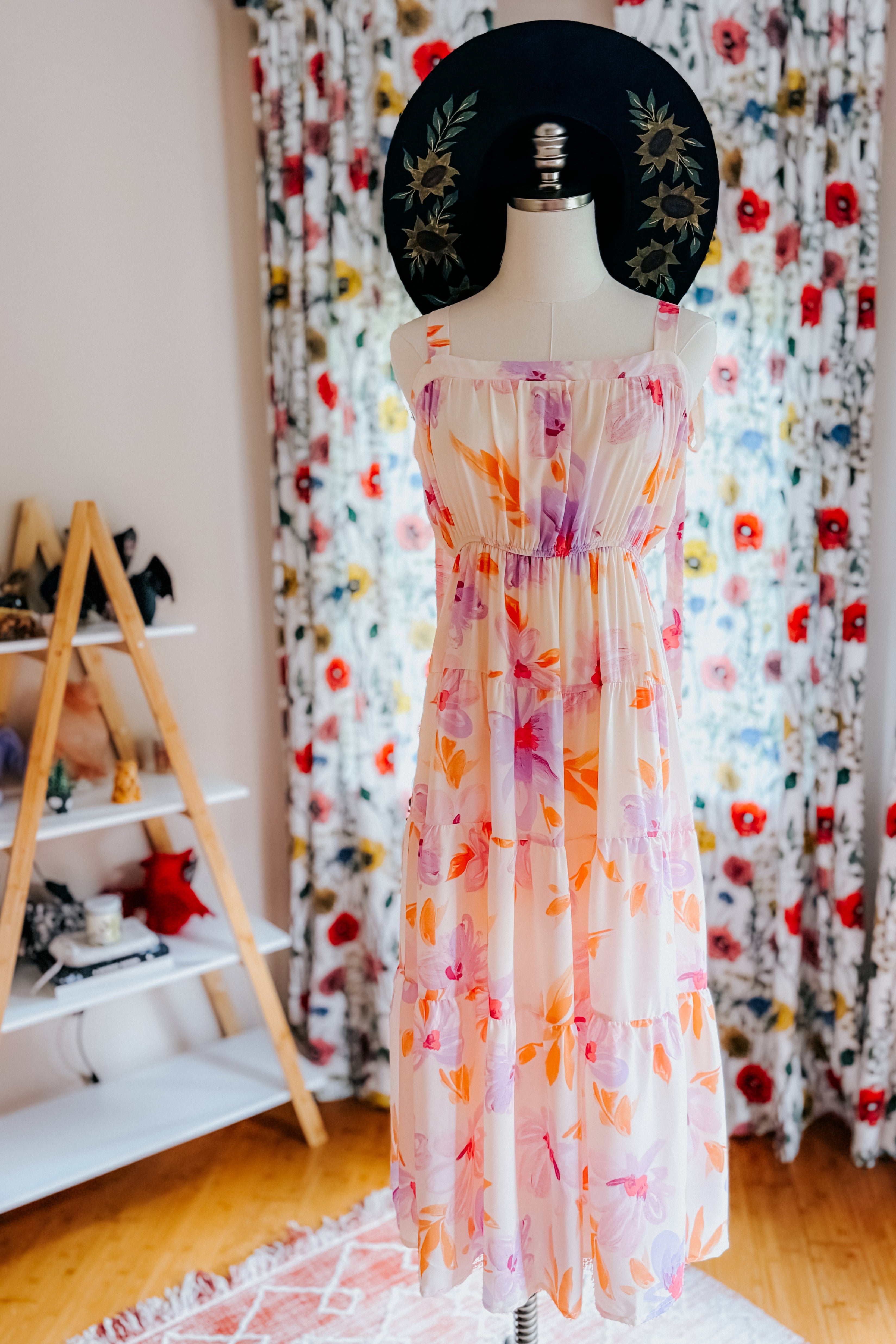 Tiered pastel peach floral dress with adjustable straps styled with embroidered wide-brim black hat indoors