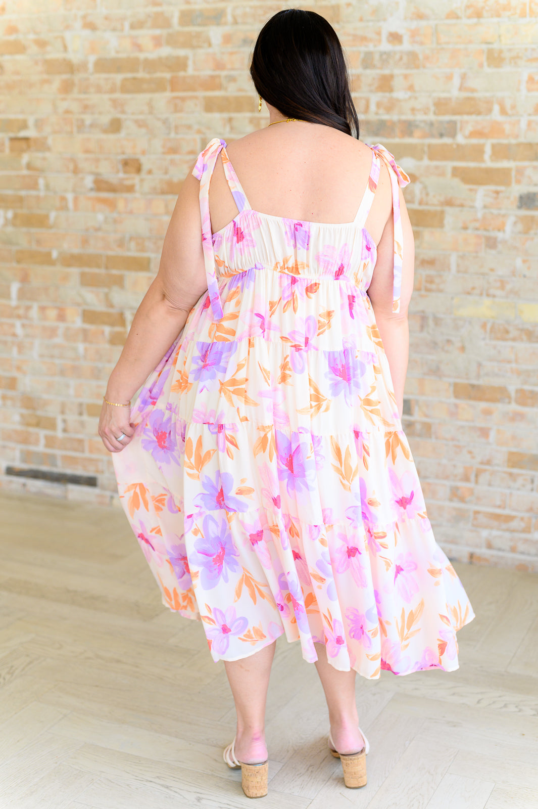 Plus-size woman wearing pastel petals floral midi dress with tie shoulder straps and block heels by brick wall
