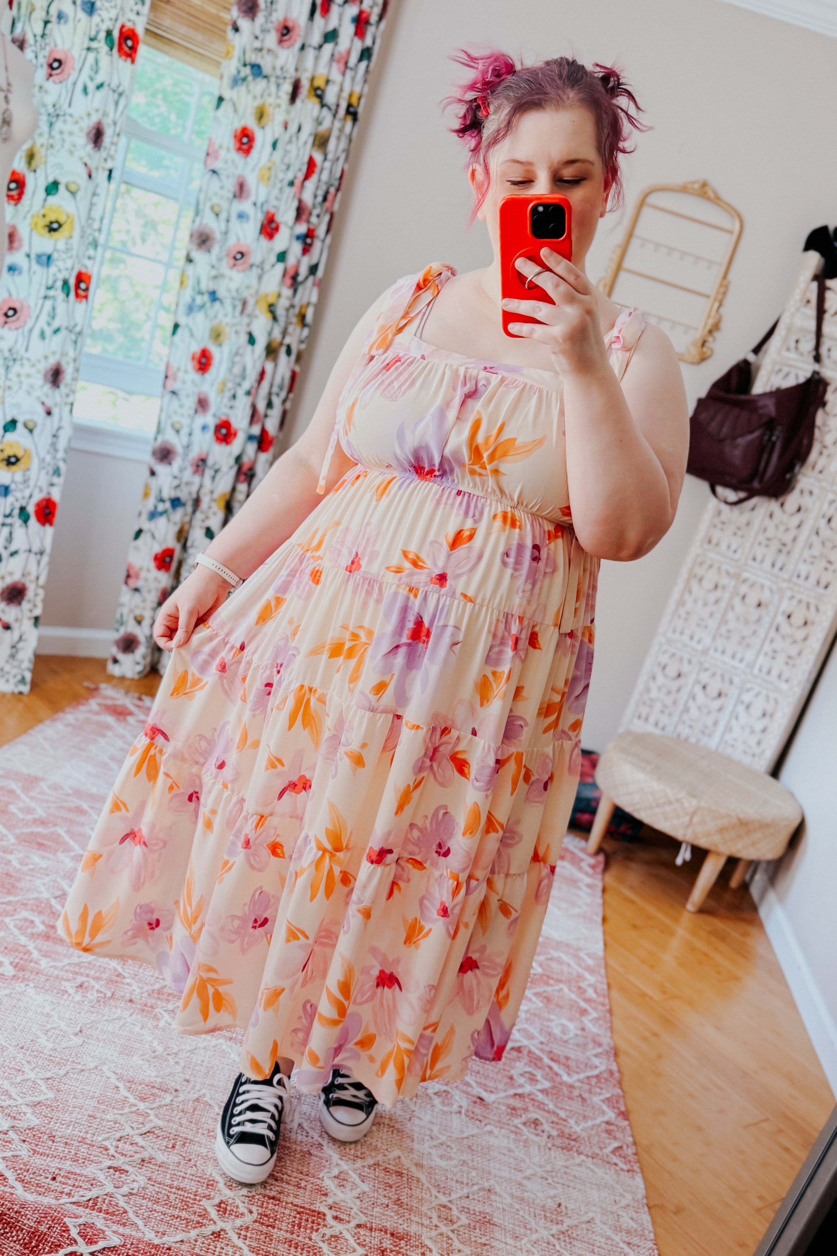 Plus-size woman with pink hair wearing peach floral midi dress with adjustable straps and black sneakers indoors