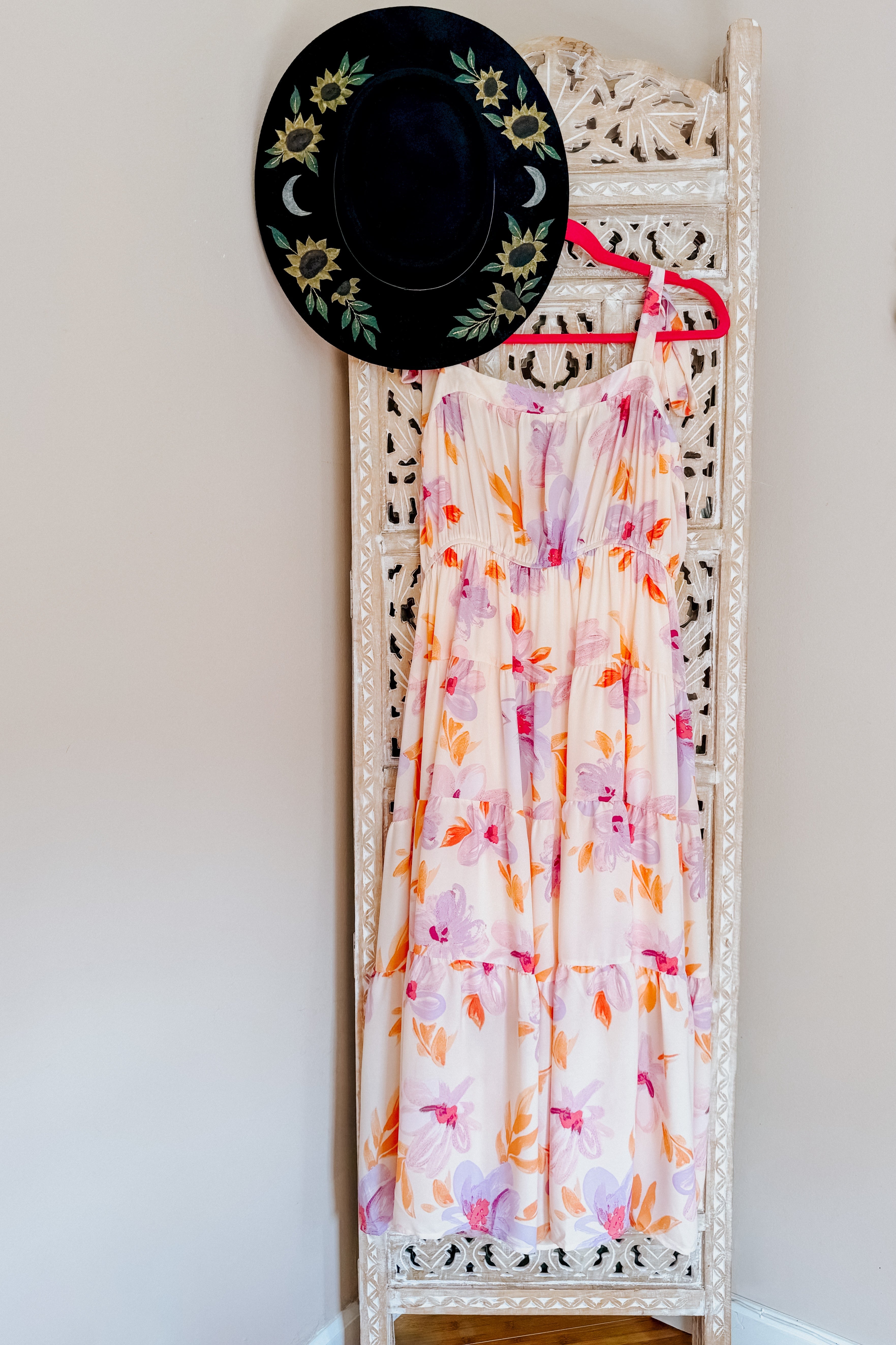 Flowy pastel petals midi dress with tie straps hanging on ornate white carved screen with black sunflower hat