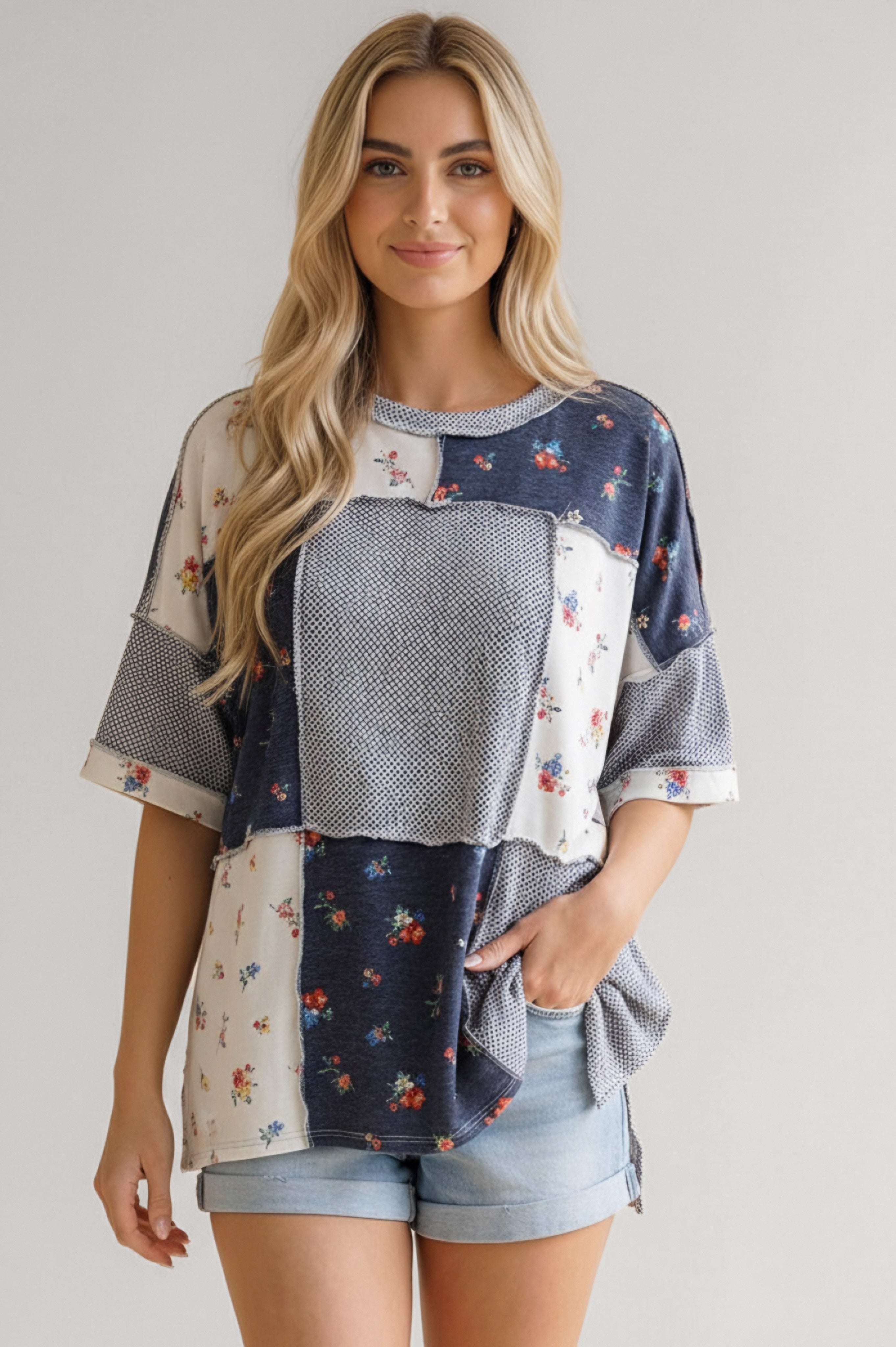 Woman wearing a loose blue patchwork top with small floral and geometric prints paired with light denim shorts